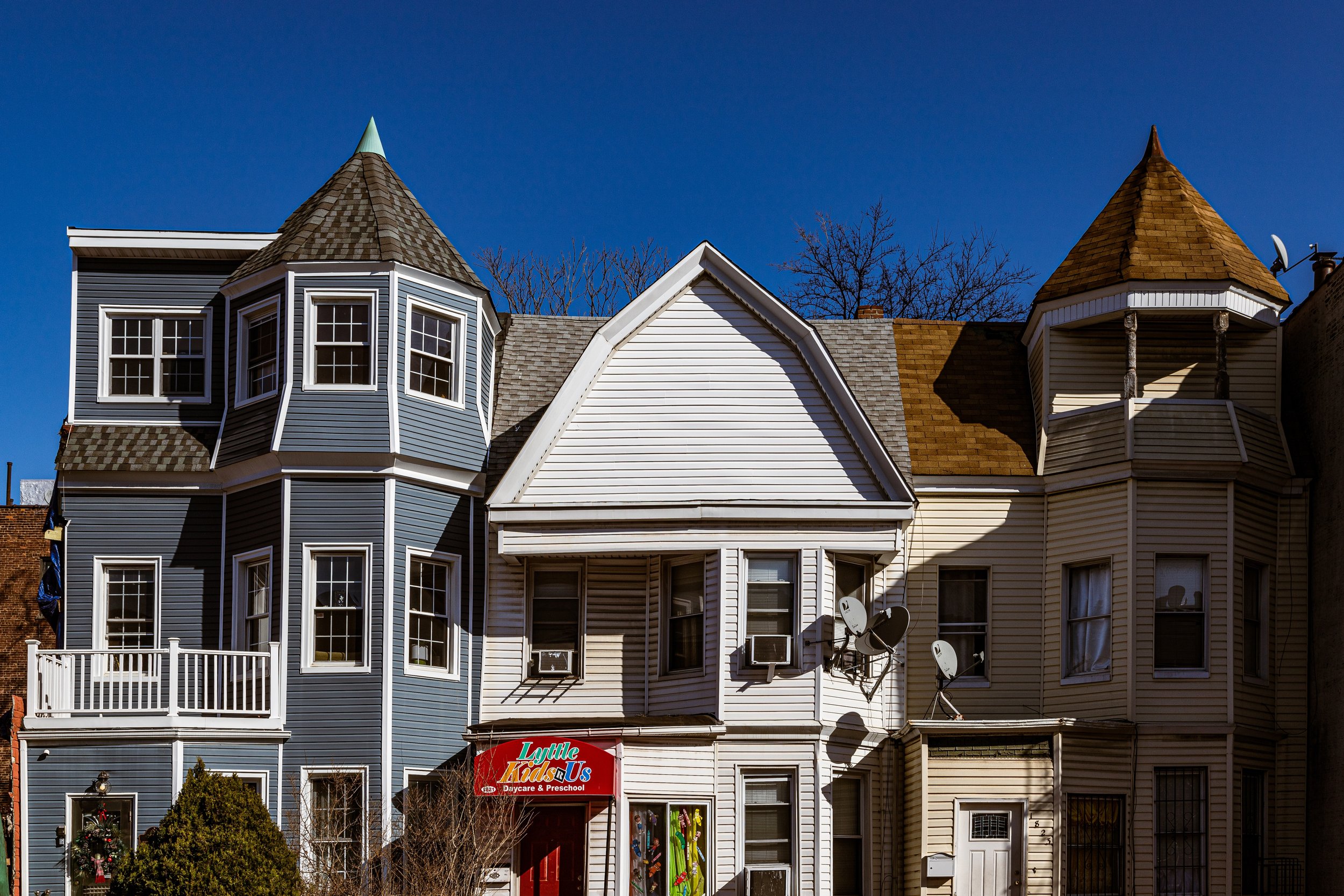 Colorful Victorian-style row house with bay windows, turrets, and a small business storefront for Little Kids U Daycare & Preschool in an urban neighborhood under a clear blue sky.