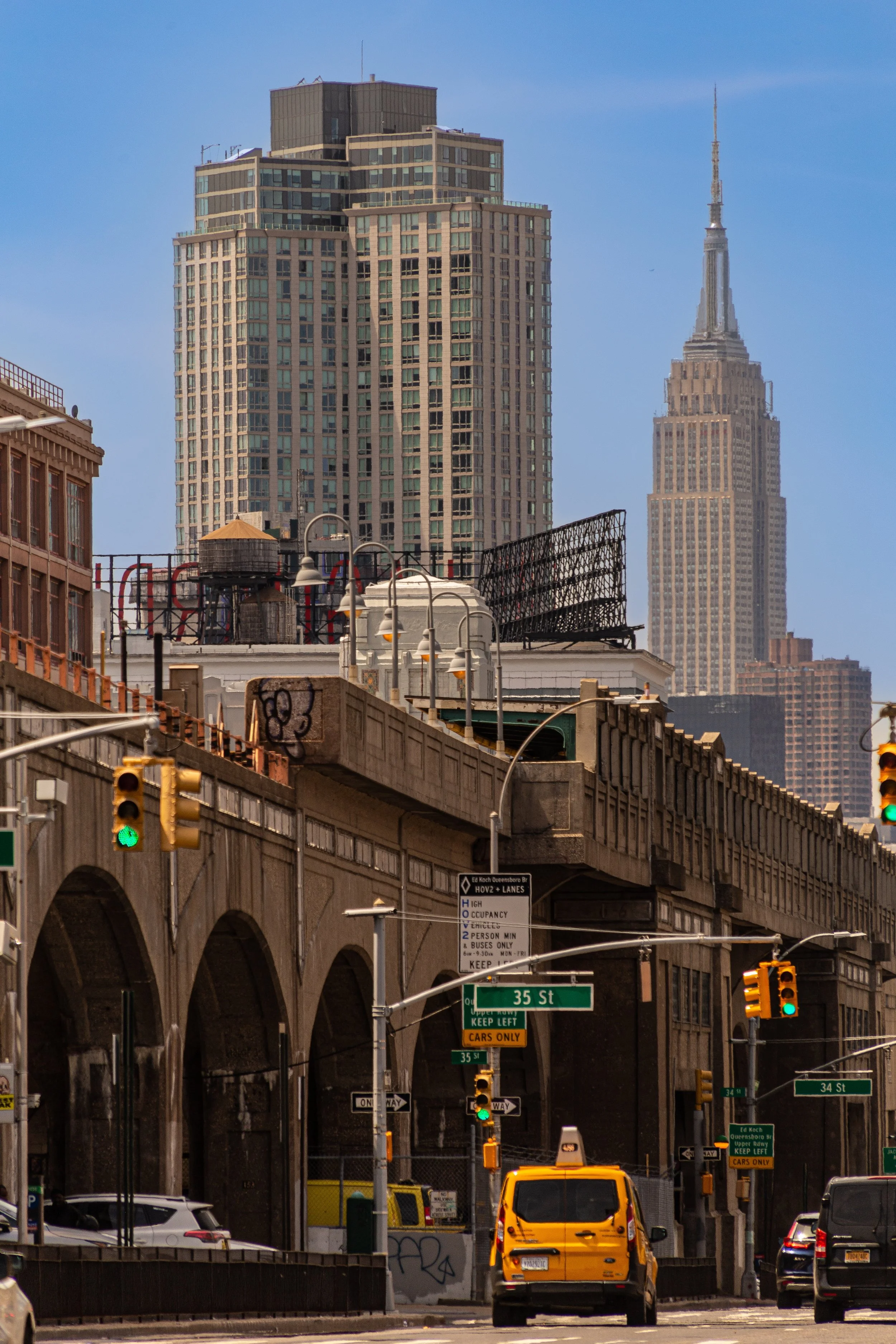 Street scene in a city with traffic lights, a yellow taxi, and tall buildings including the Empire State Building in the background.