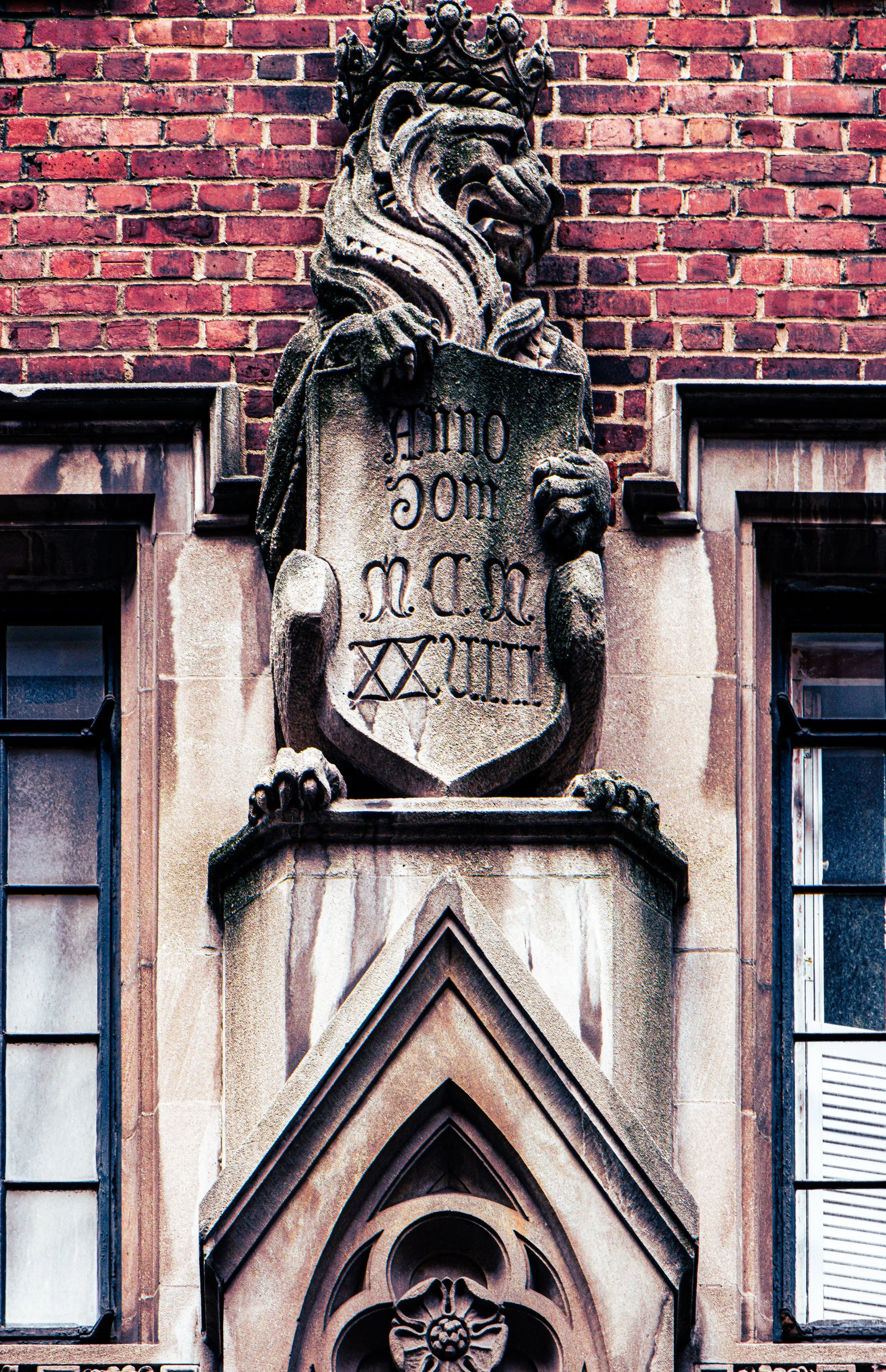 Stone sculpture of a lion wearing a crown, holding a shield with inscriptions, mounted on a brick and stone building façade.
