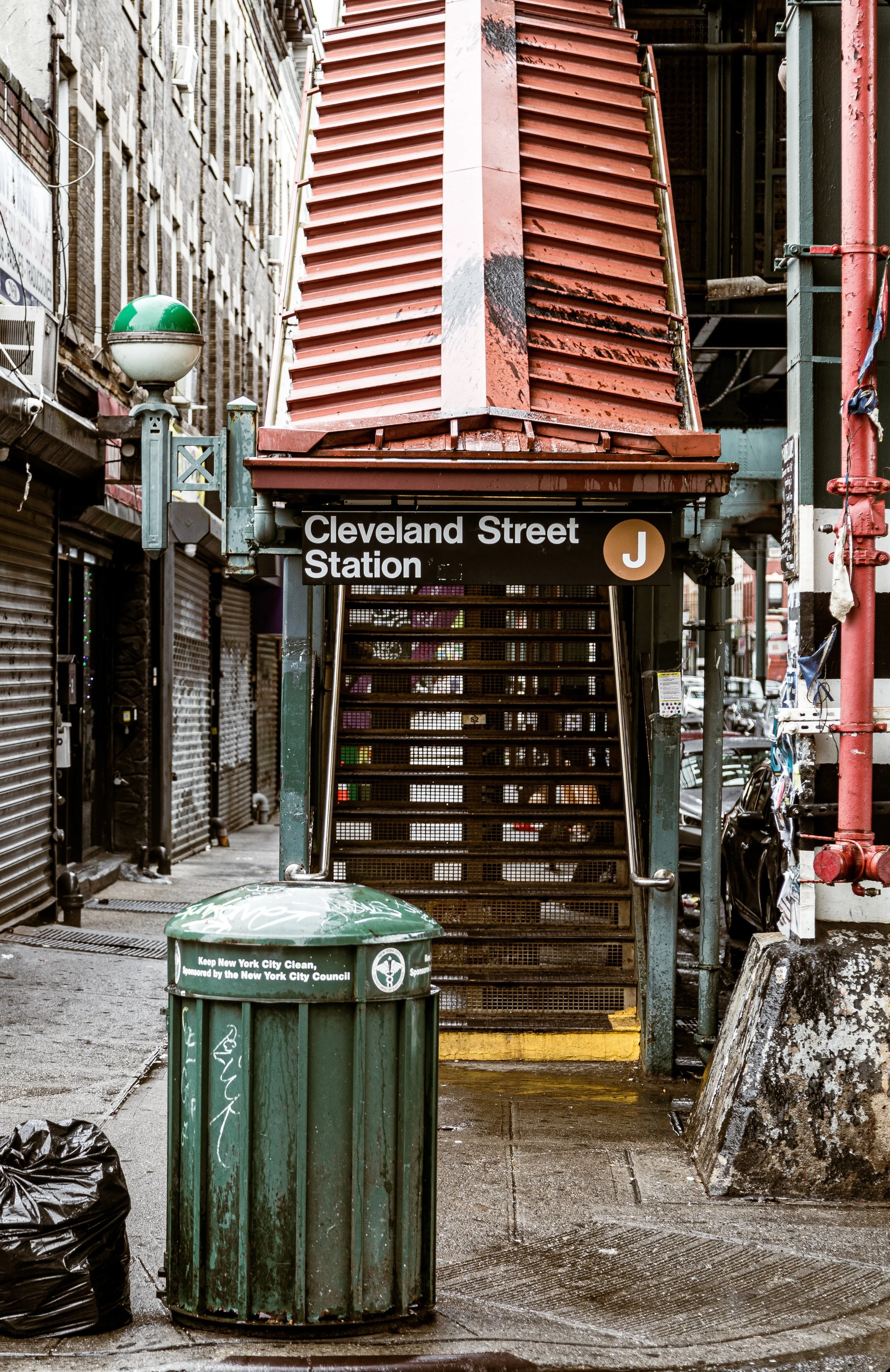 Street view of Cleveland Street Station entrance with stairs, sign, and surrounding urban elements in New York City.