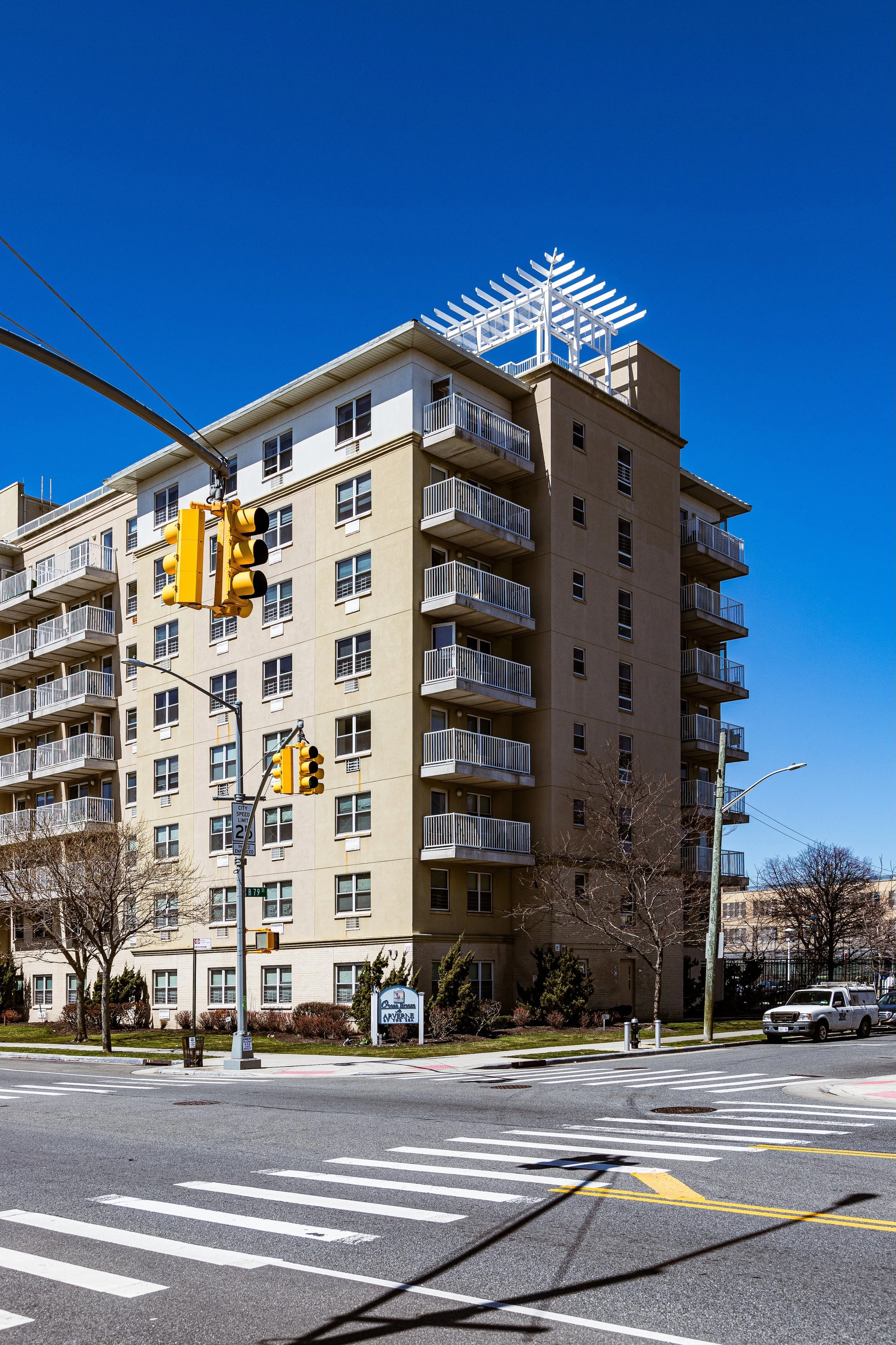 A multi-story apartment building with balconies, traffic lights, and a clear blue sky at a city intersection.