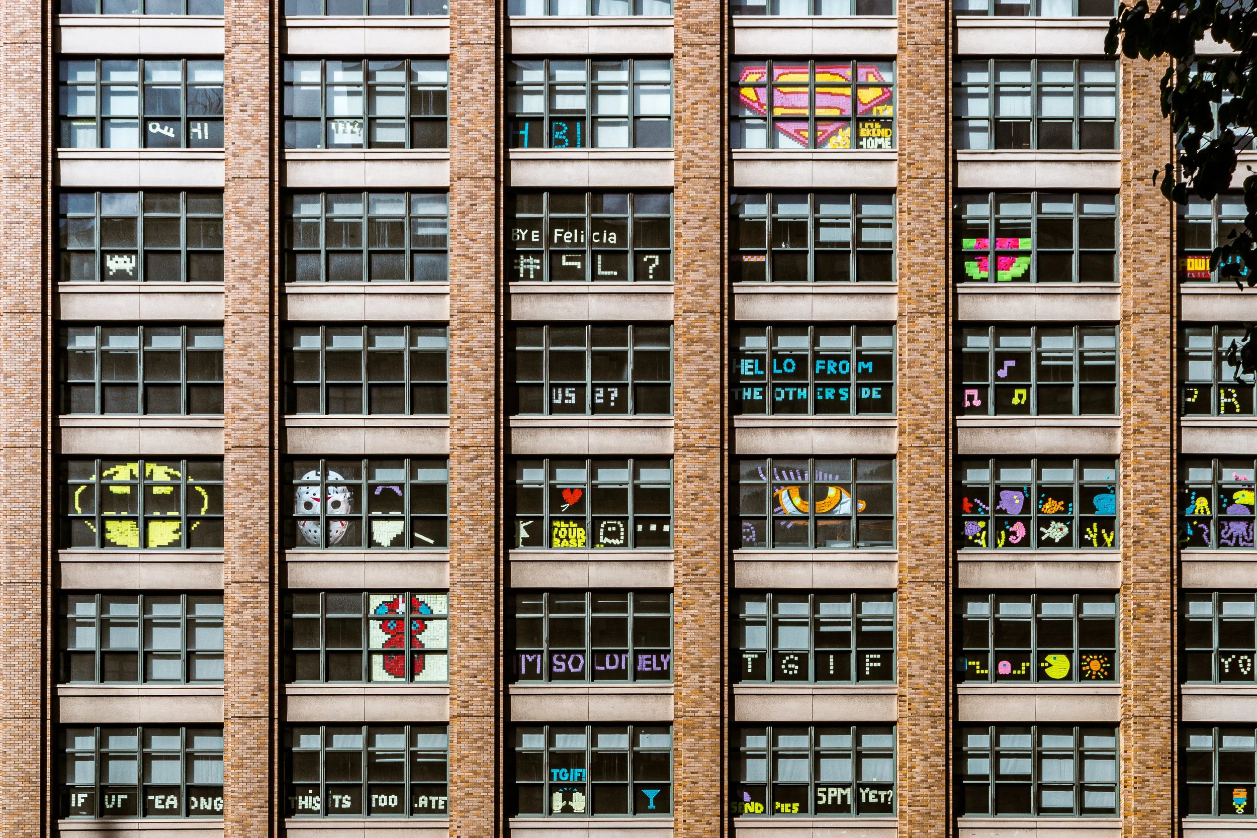 Windows of a brick building with digital art and messages displayed on the windows, resembling pixel art and video game graphics.