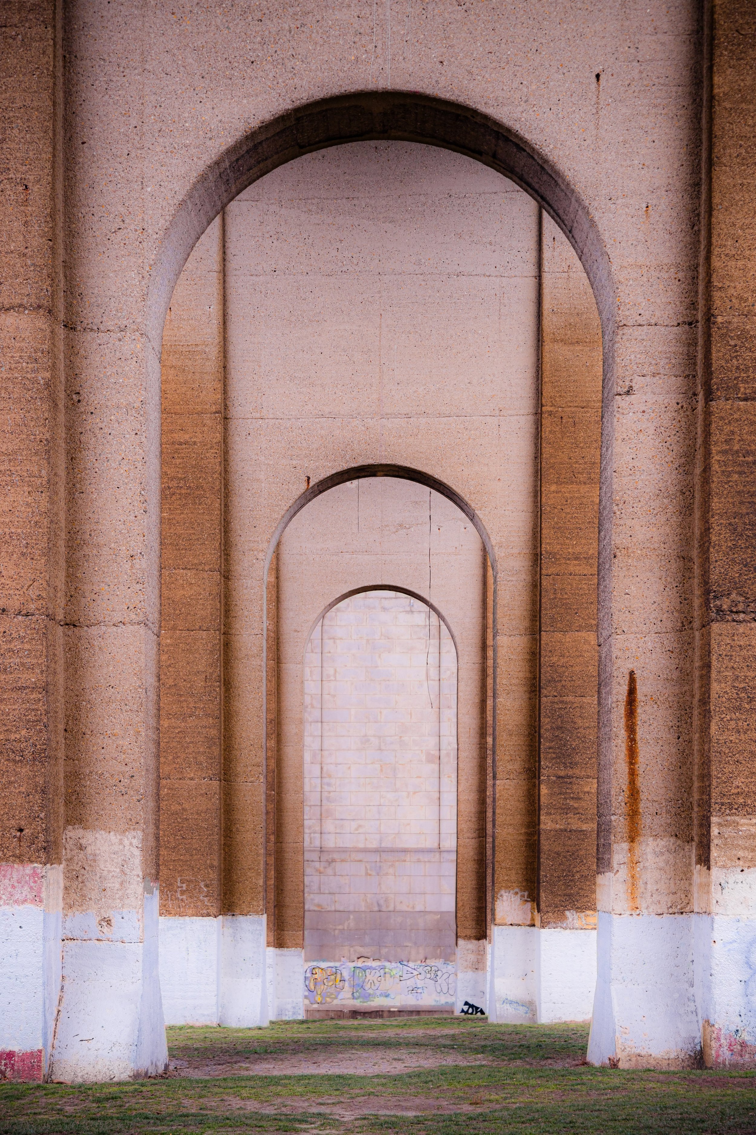 Multiple large stone arches in a series, with graffiti at the base, and a grassy ground underneath.