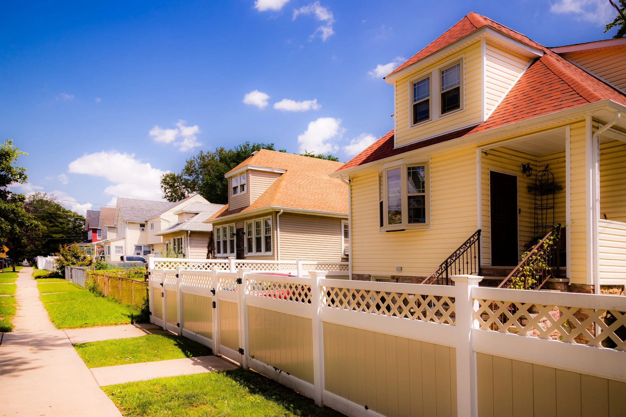 Suburban neighborhood with colorful houses, white fences, and a sunny sky.