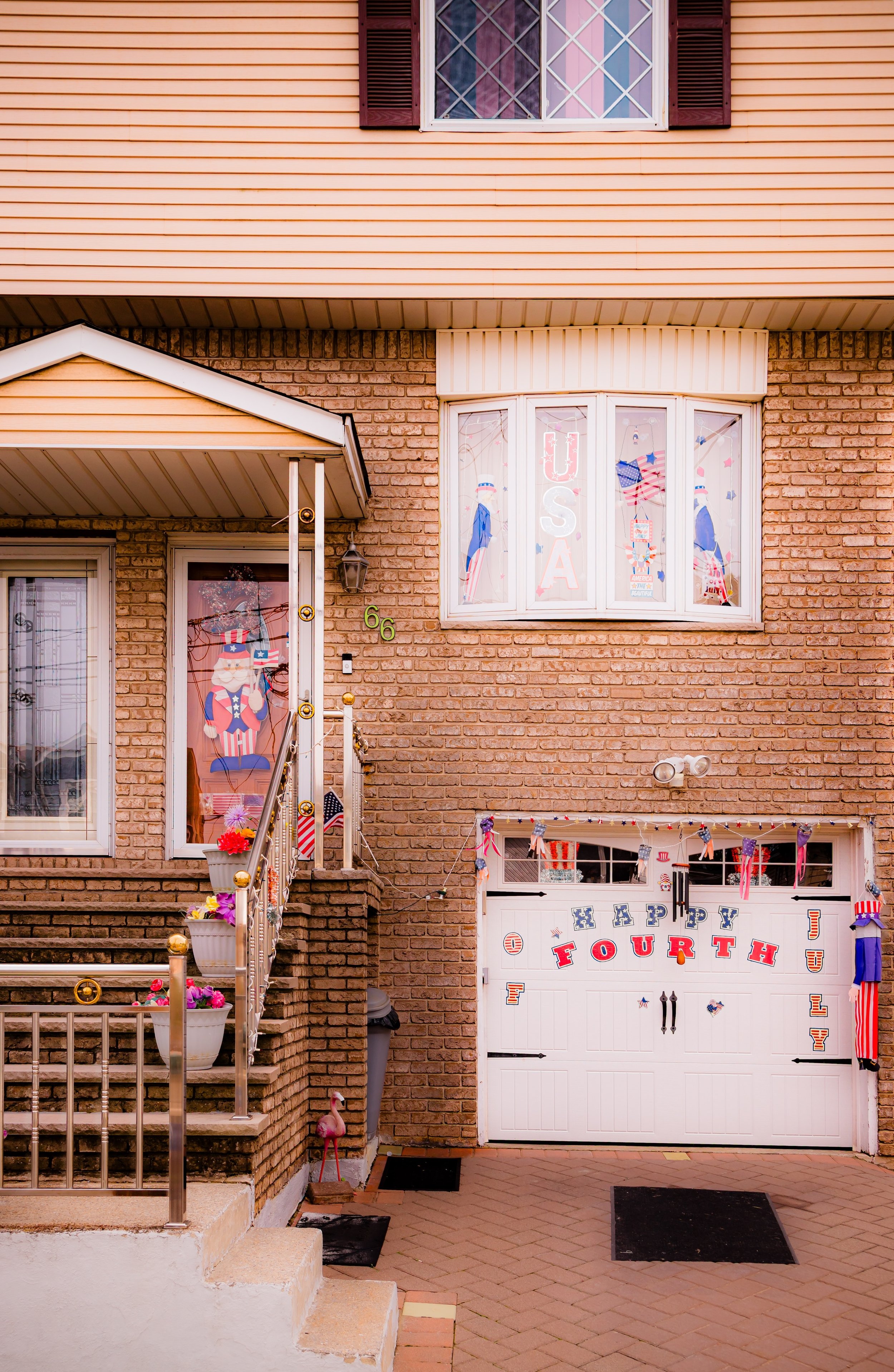 A house decorated for the Fourth of July with patriotic banners, flags, and a 'Happy Fourth' sign on the garage door, featuring red, white, and blue colors and Uncle Sam flags.