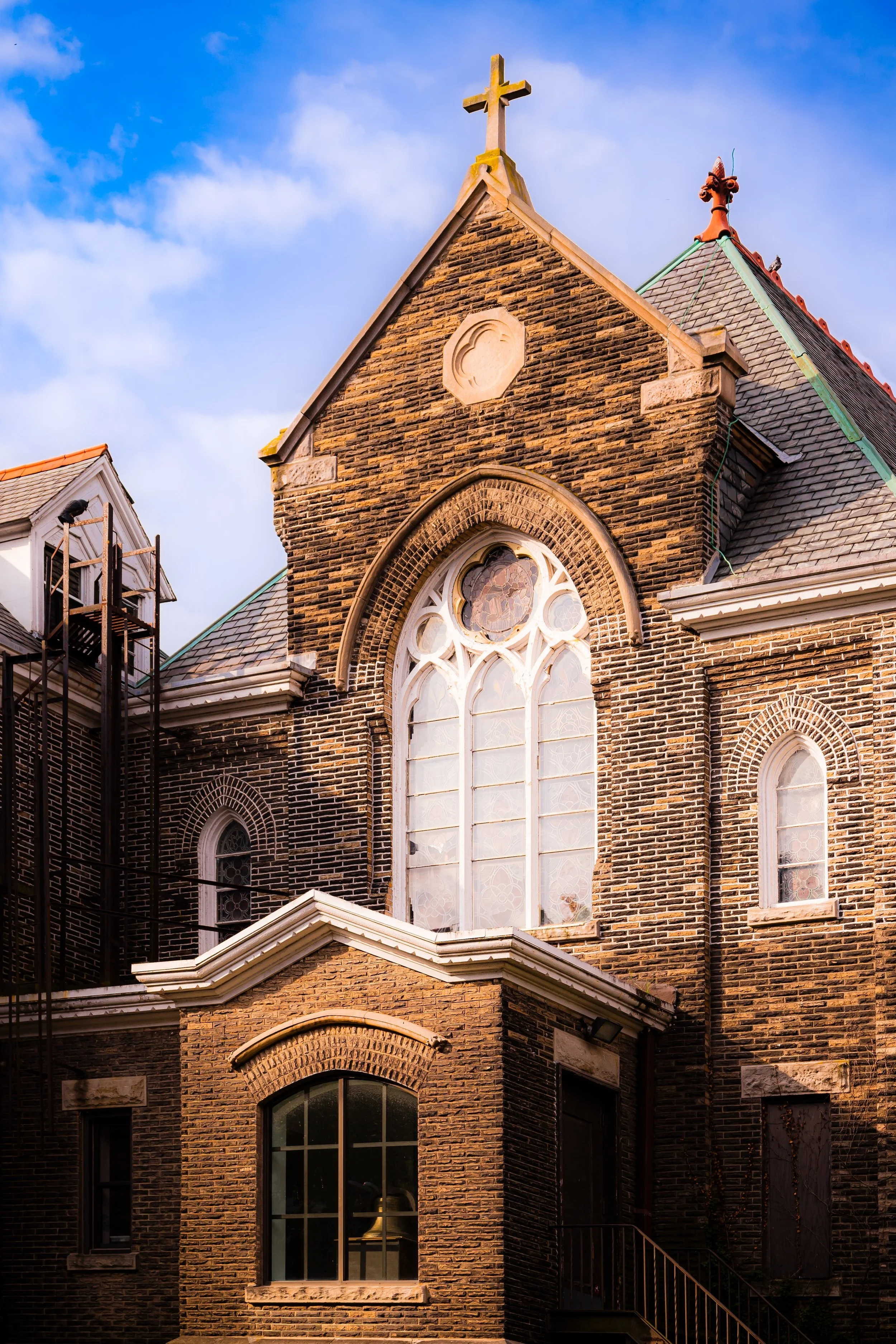 A close-up view of a brick church building with stained glass windows and a cross on top, under a partly cloudy sky.