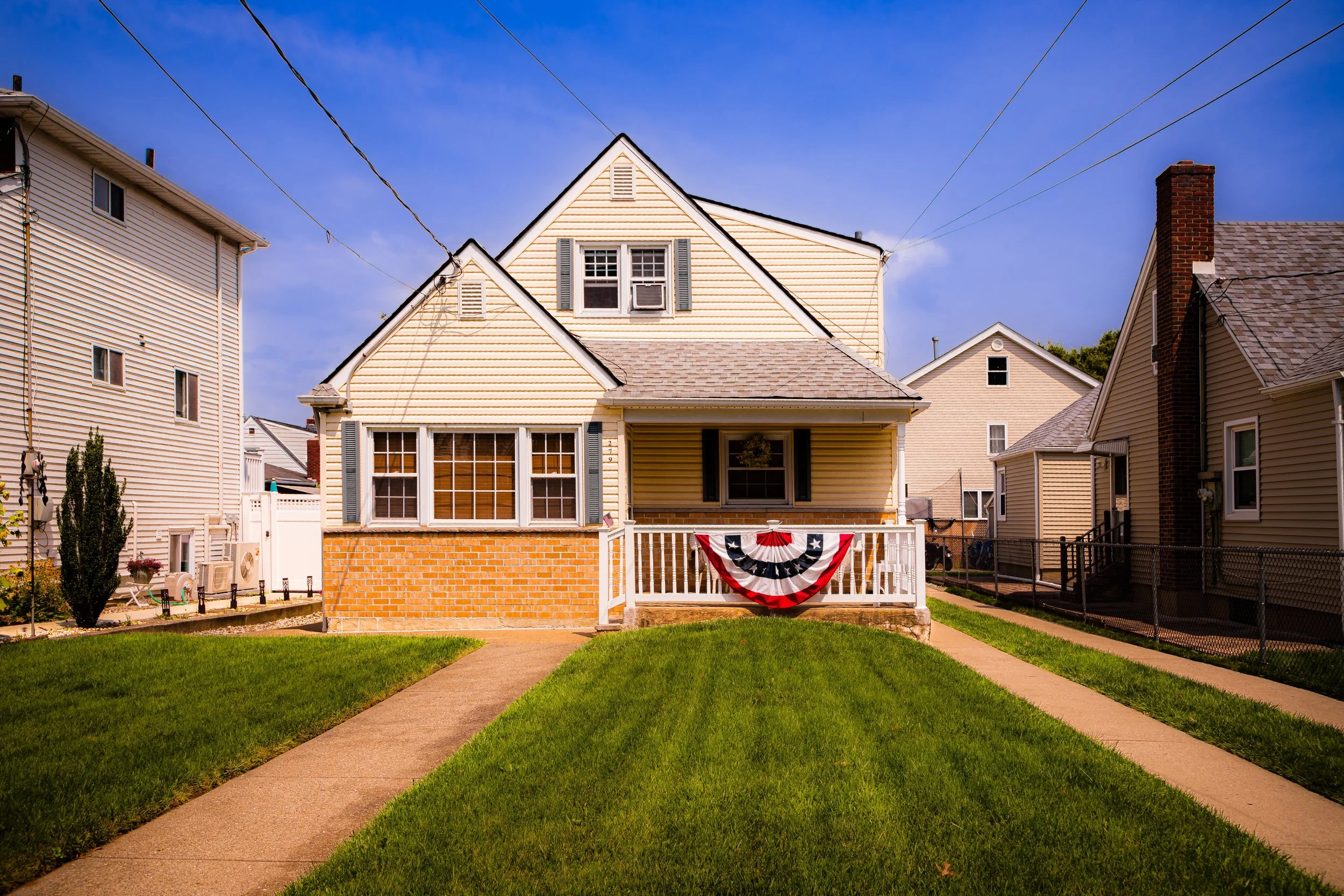 Front view of a house decorated with a red, white, and blue bunting, surrounded by neighboring houses on a sunny day.