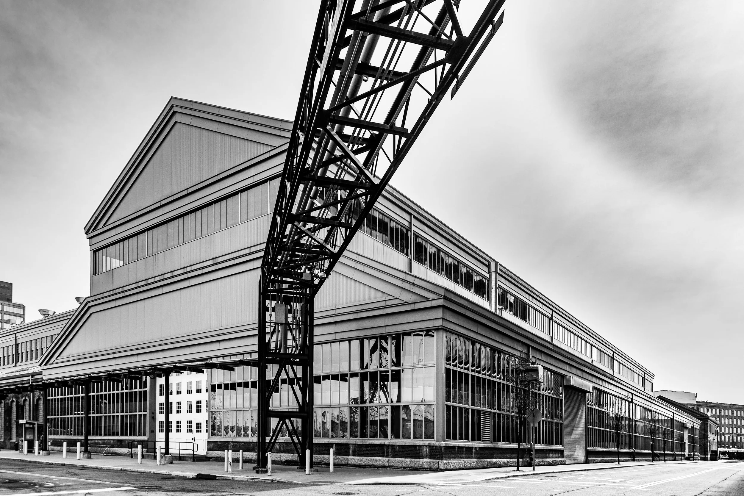 Black and white photo of a modern industrial building with large glass windows and an adjacent metal tower structure.