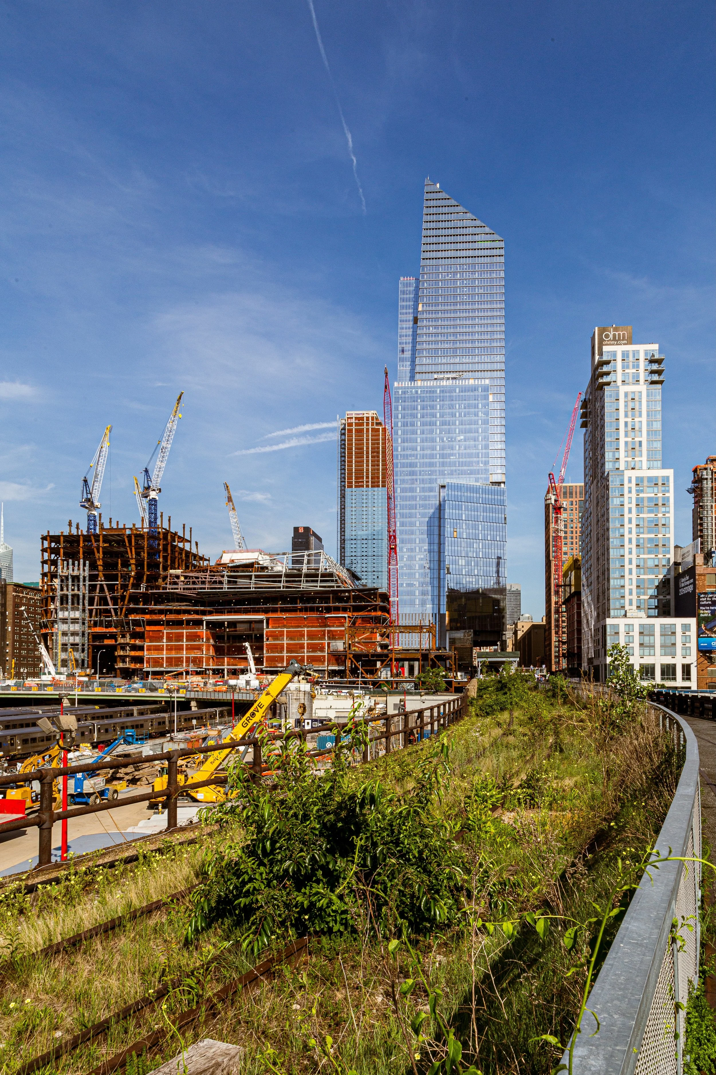 Construction site with cranes and partially built skyscraper in downtown city, with a clear blue sky overhead.
