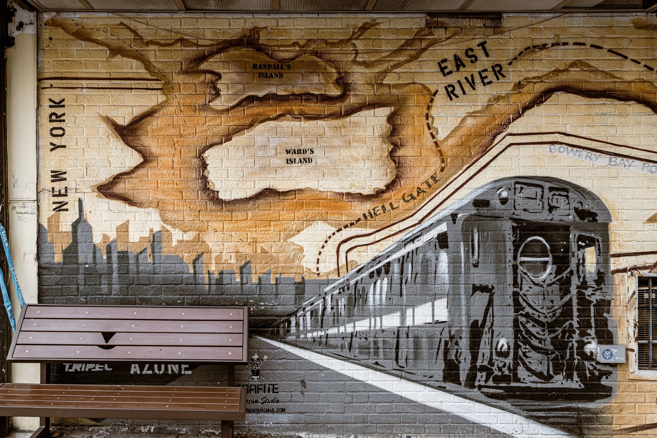 Wall mural of a New York City subway train approaching a station with a city skyline silhouette and map of the East River, Randall's Island, Ward's Island, and Bowery Bay area.