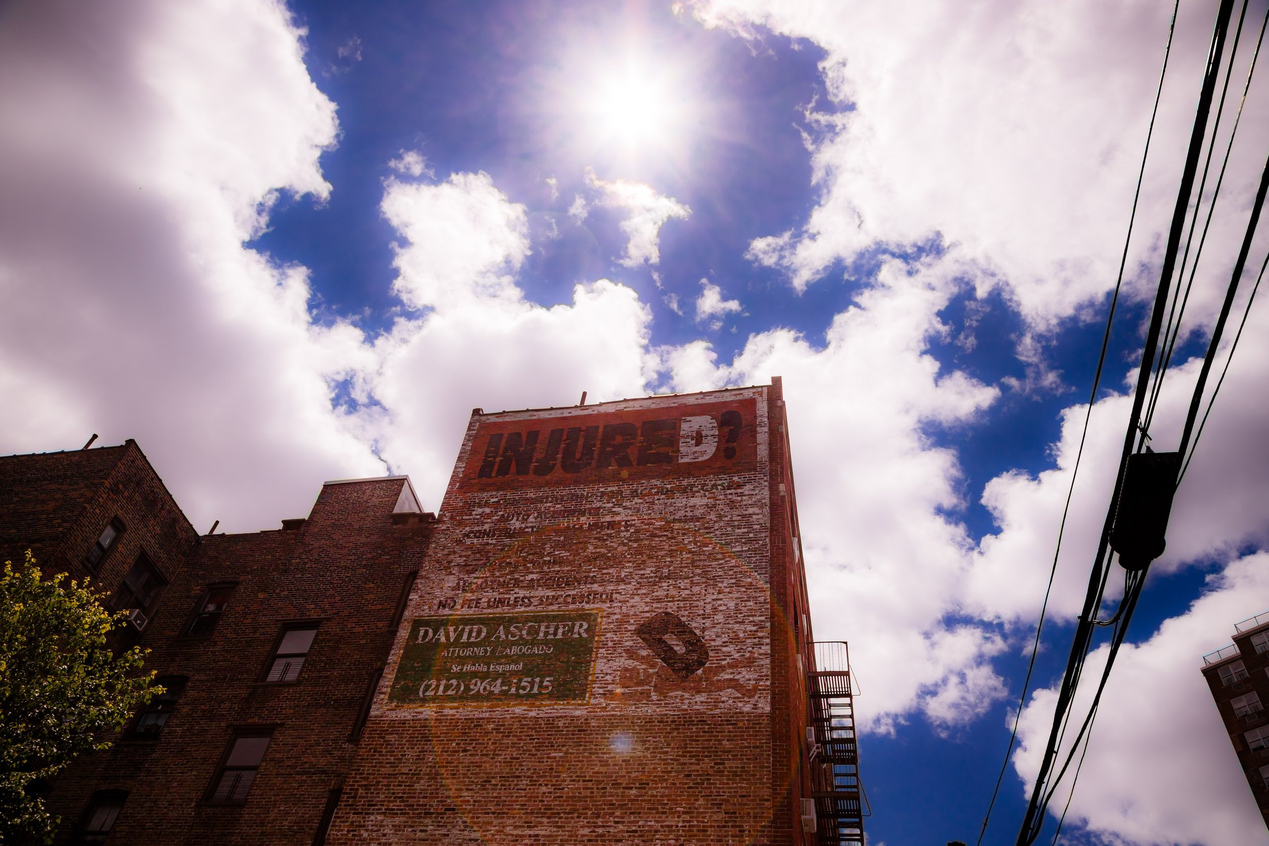 Tall brick building with a weathered advertisement that reads 'INJURED?' under a partly cloudy sky with the sun shining overhead.