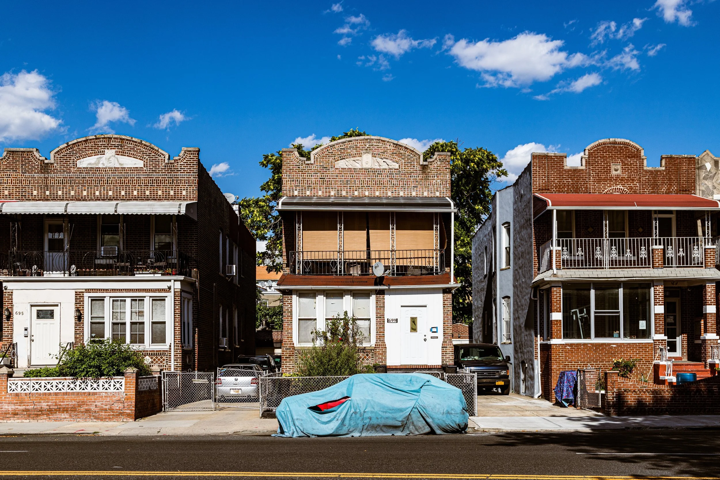 Three residential brick houses with front porches on a sunny day under a blue sky with clouds.