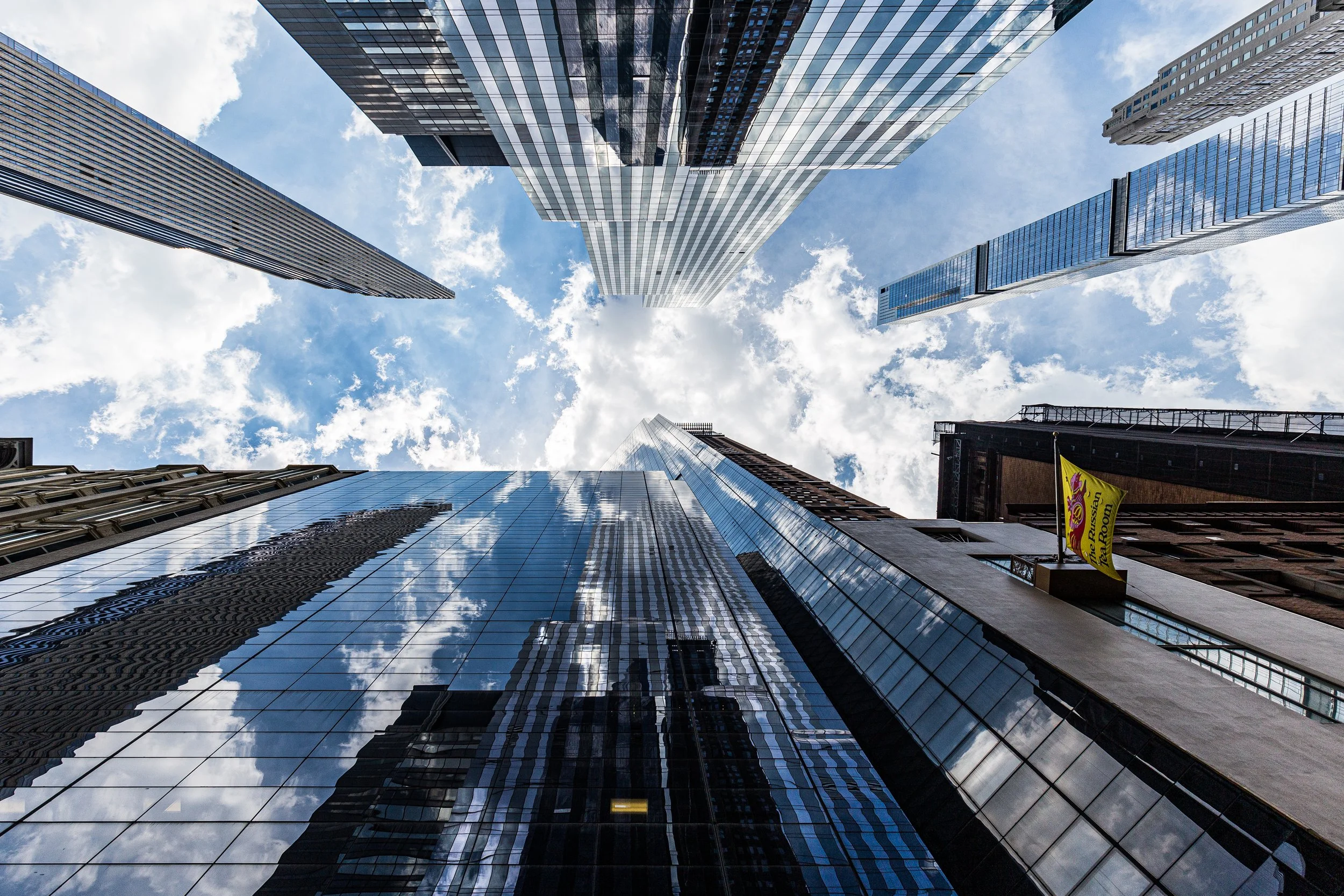 Looking up at tall modern skyscrapers with glass facades reflecting the sky and clouds.