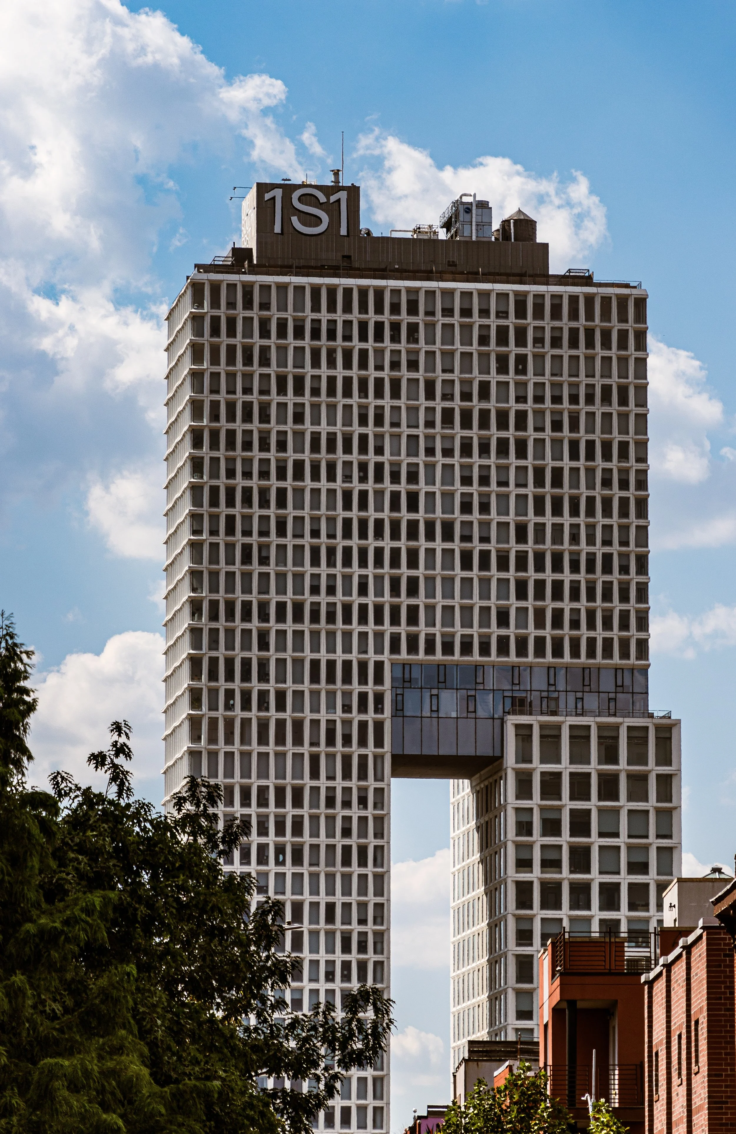 A tall modern building with a rectangular, open middle section, covered in square windows, under a partly cloudy sky.