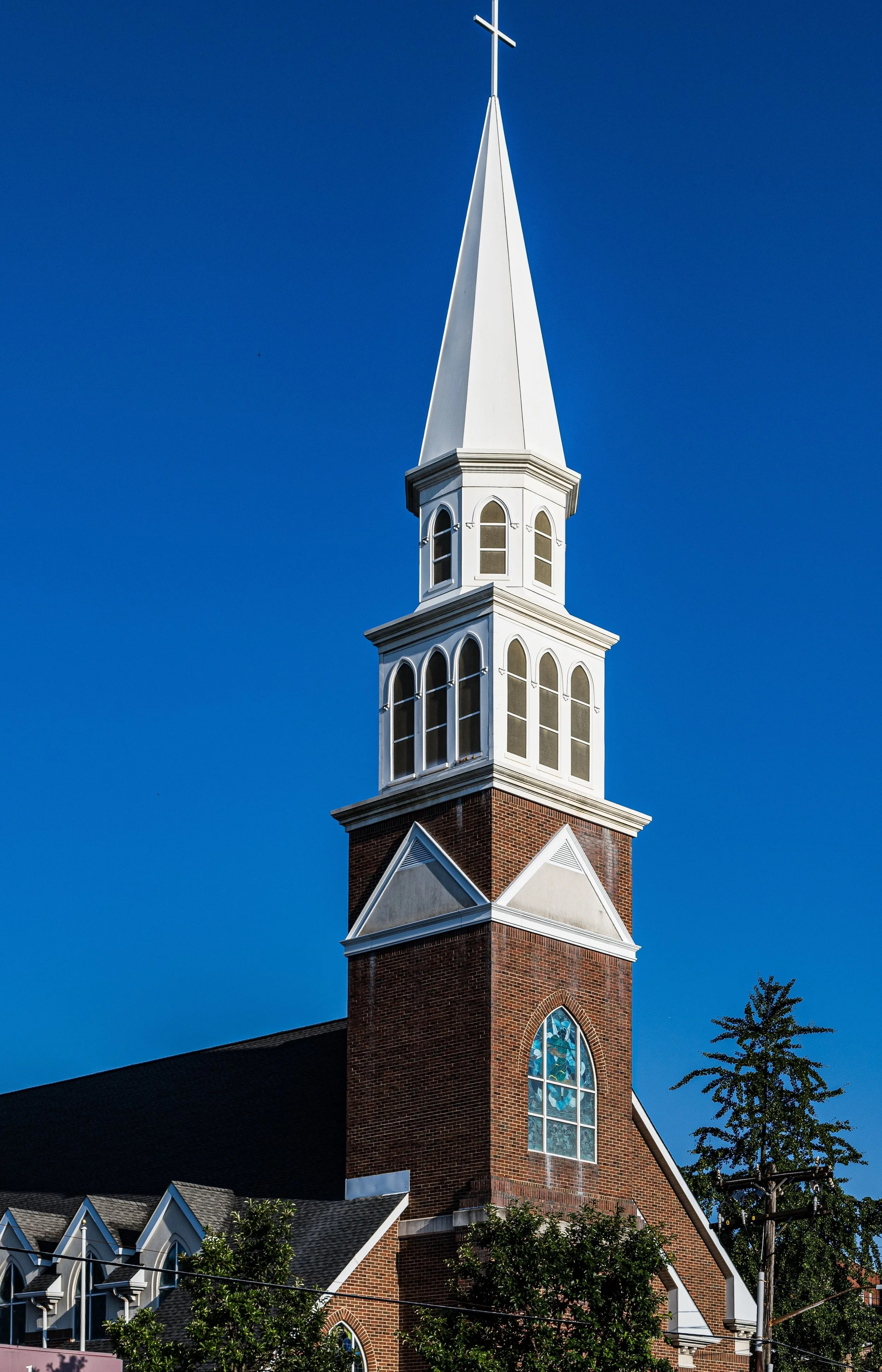 A church steeple with a cross at the top, against a clear blue sky.