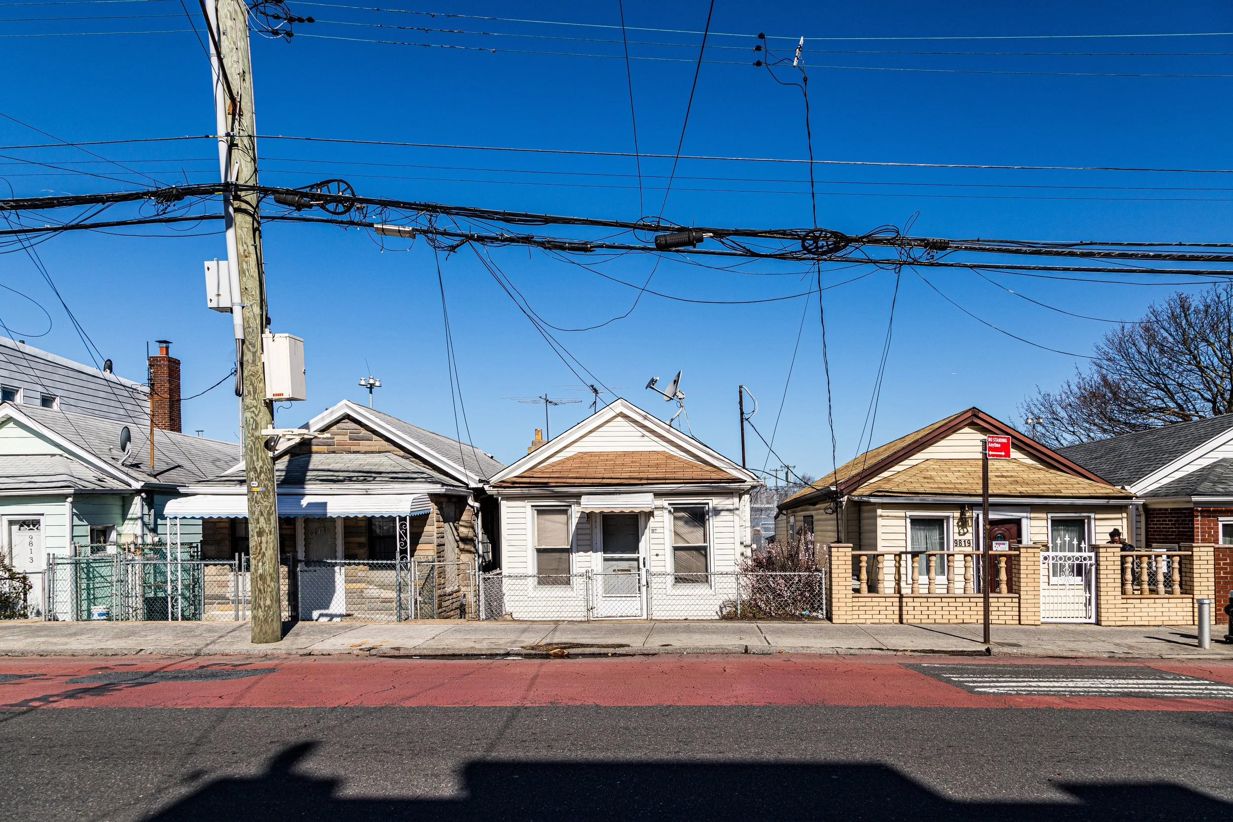 Row of small houses with different exterior designs and a power pole with tangled overhead wires against a clear blue sky.