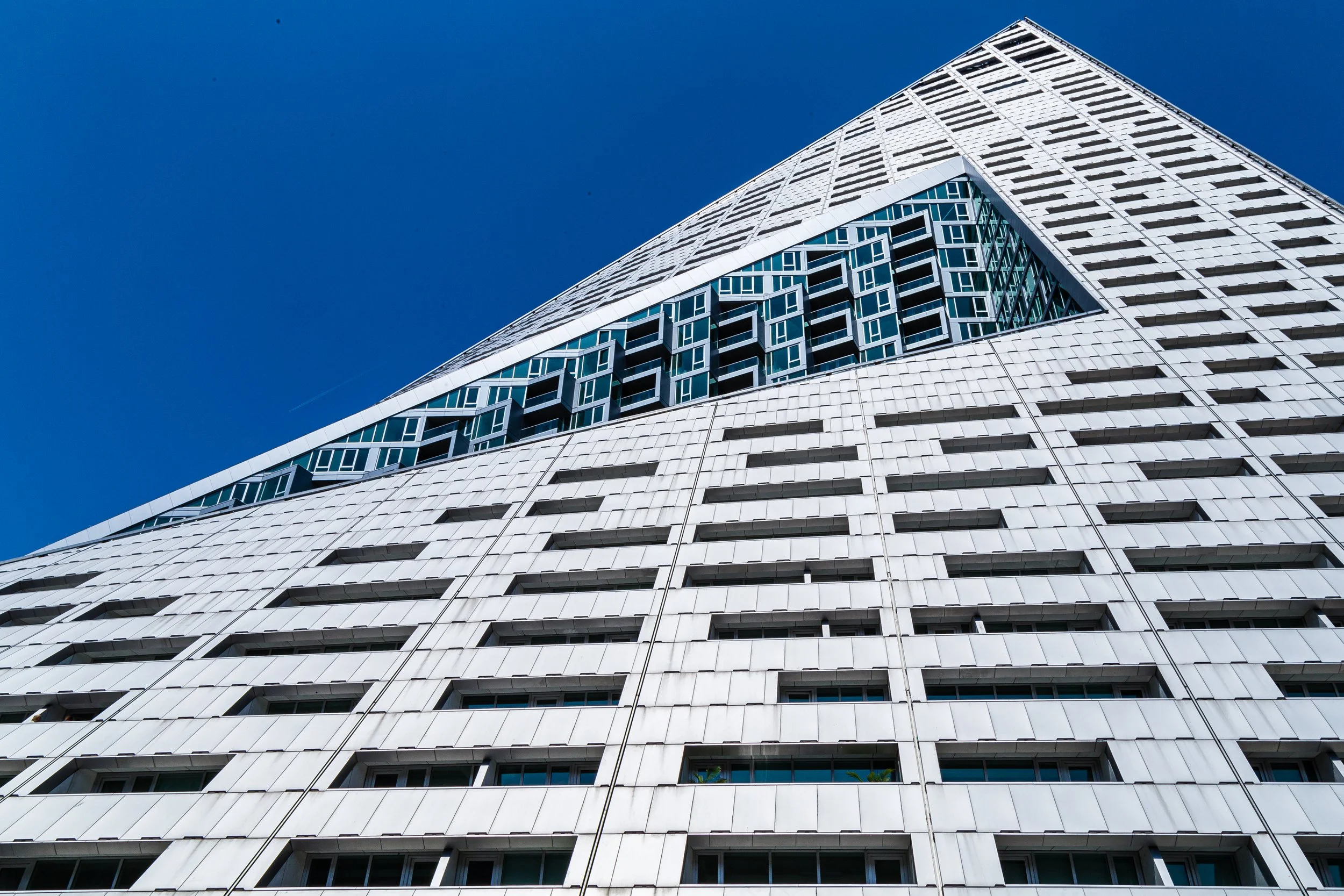 Low-angle view of a modern white high-rise building with a geometric design against a clear blue sky.