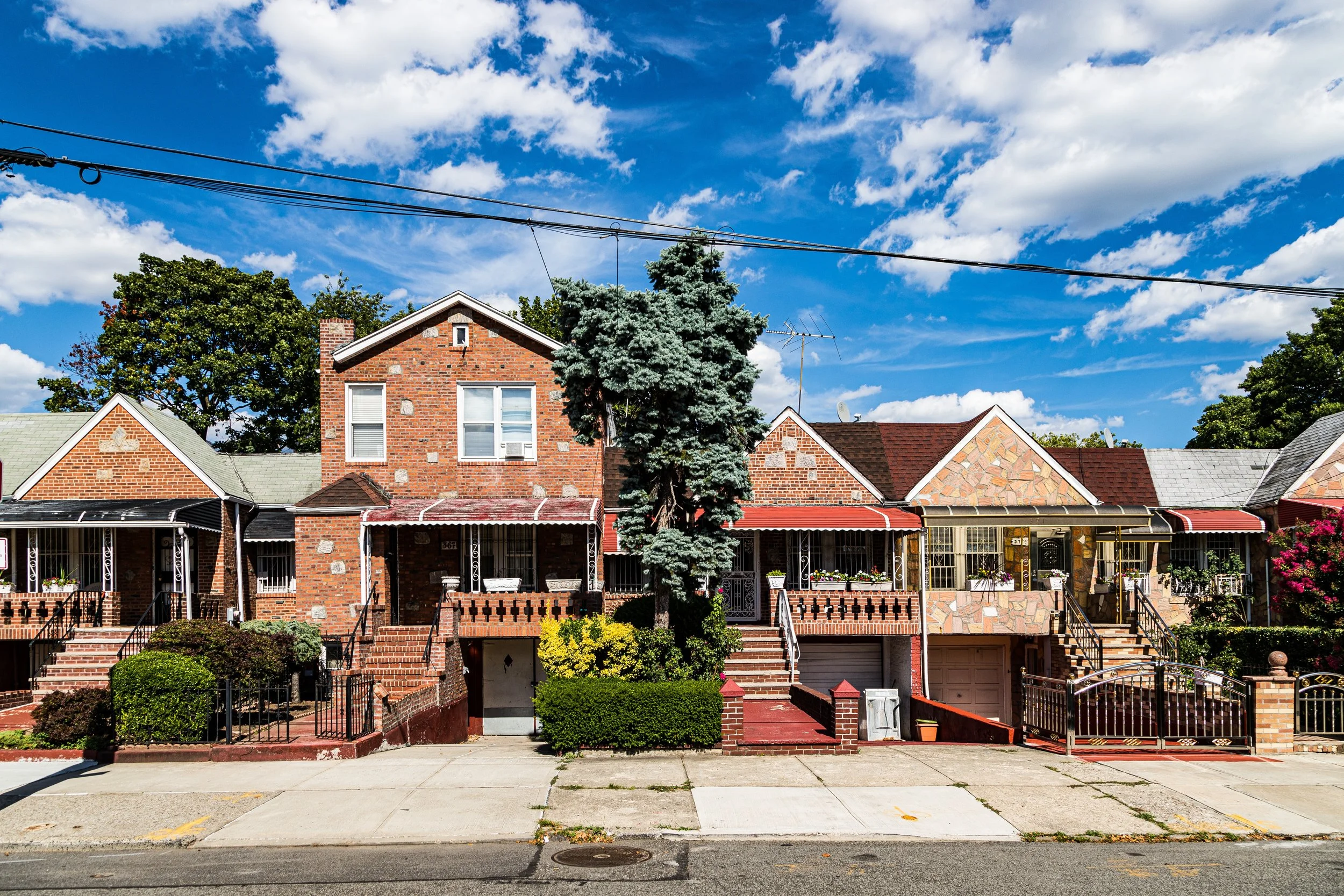 Row of brick houses on a sunny day with a blue sky and white clouds, with trees and stairways leading to the entrances.