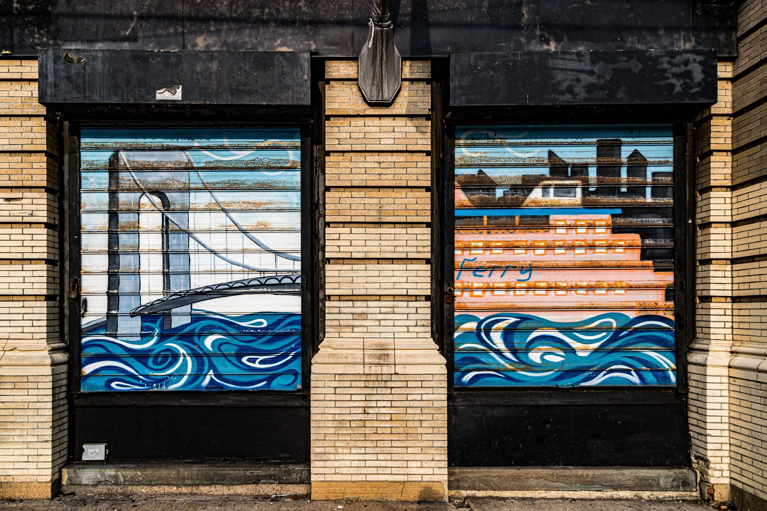 Street art mural painted on closed metal shutters depicting a bridge and water waves with buildings in the background.