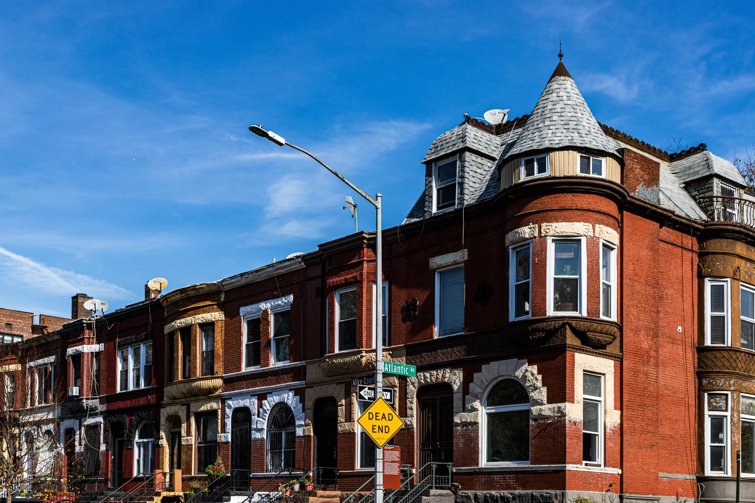A historic red brick building with bay windows, dormer windows, and a turret, located at the corner of Atlantic Avenue and Alice Court, with a 'Dead End' street sign in front.