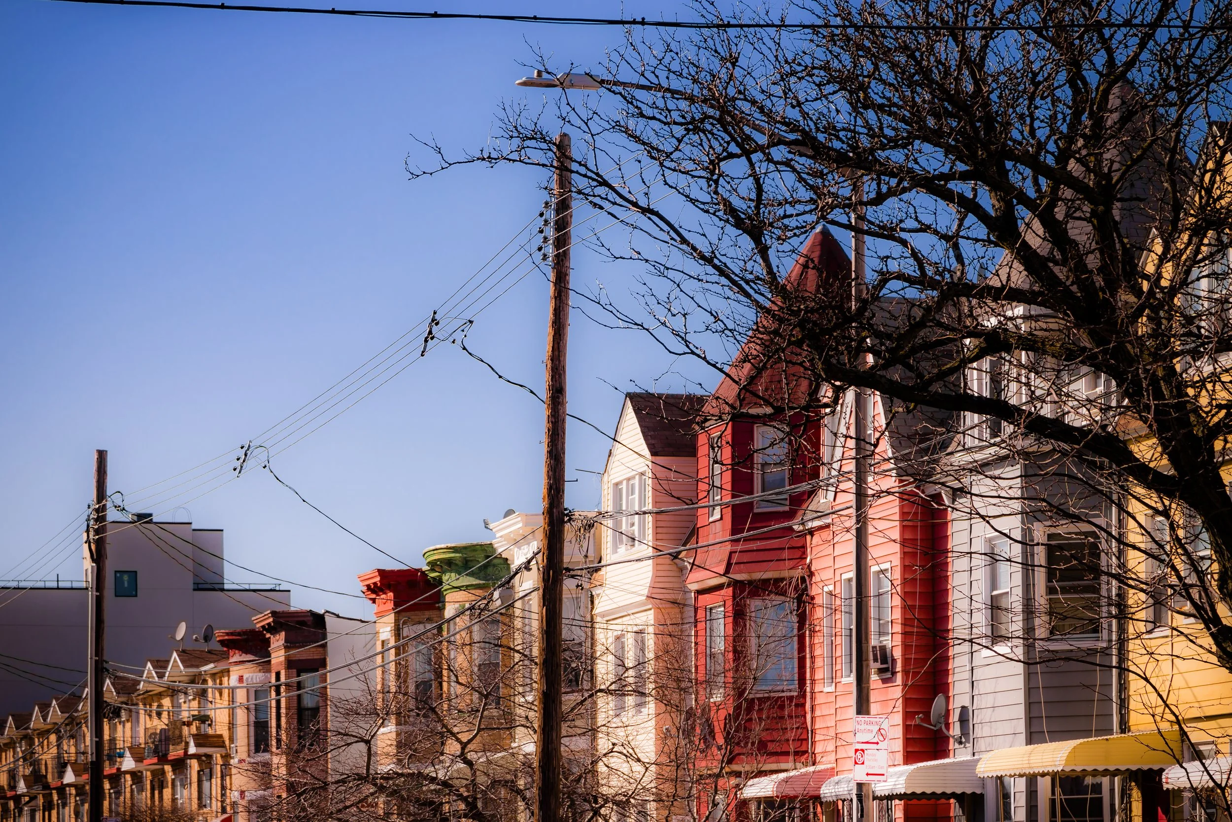 Row of colorful houses under a clear blue sky, with a leafless tree and utility poles in the foreground.