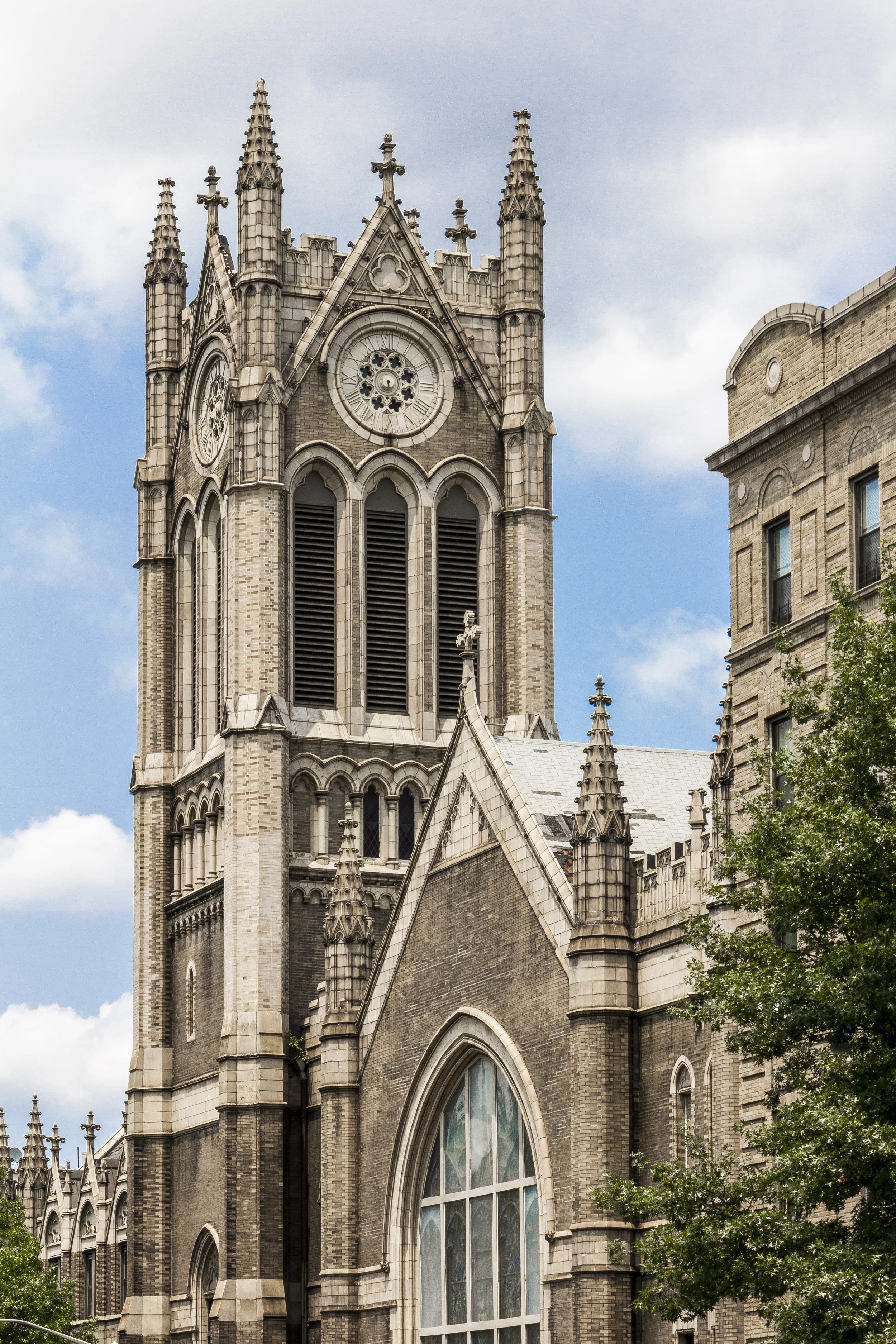 A tall, Gothic-style church with ornate spires, arched windows, and a large circular clock on the tower, set against a partly cloudy sky.