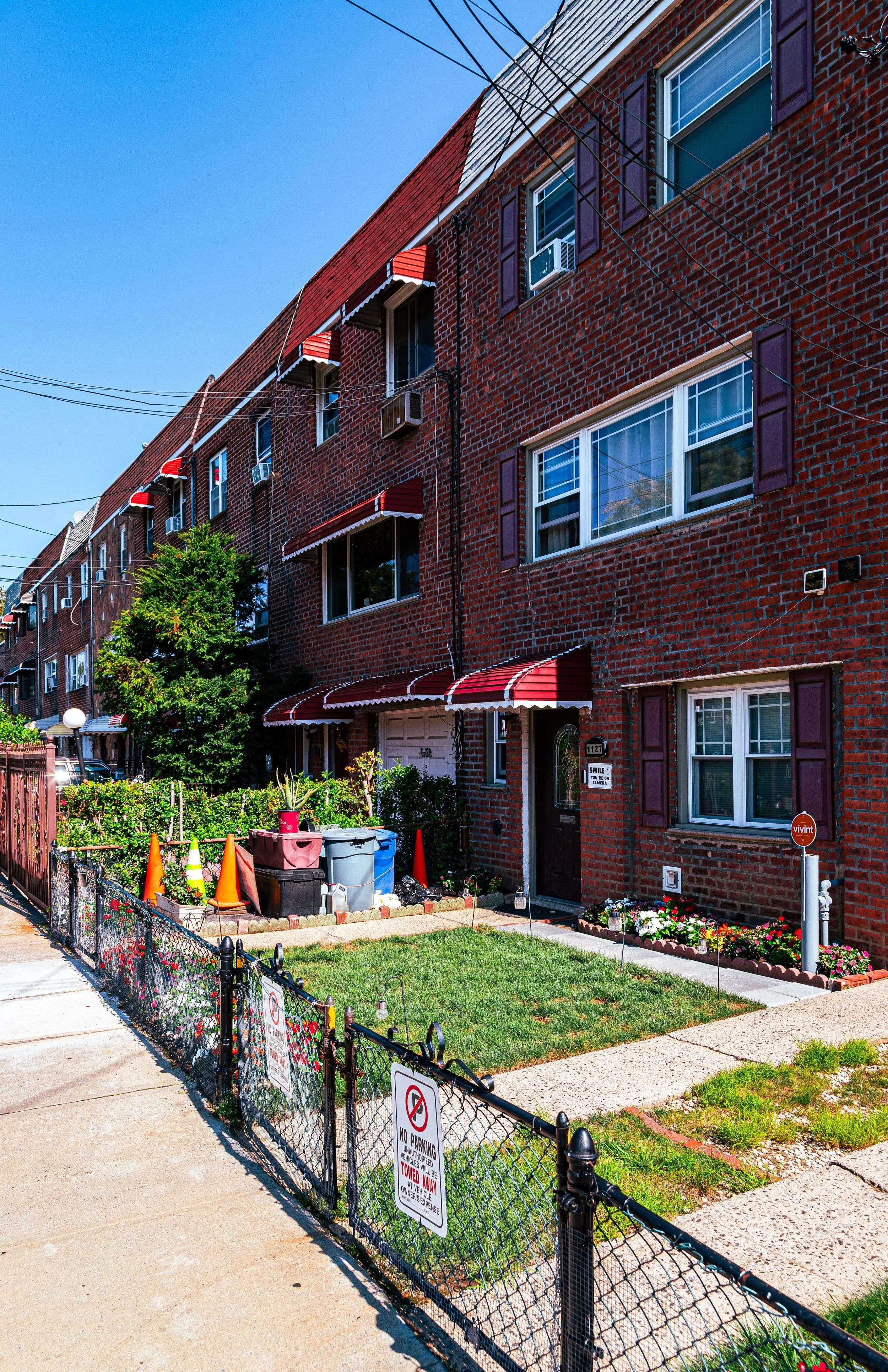 A brick residential building with small front yard, green grass, parking sign, and flower bed, on a sunny day.