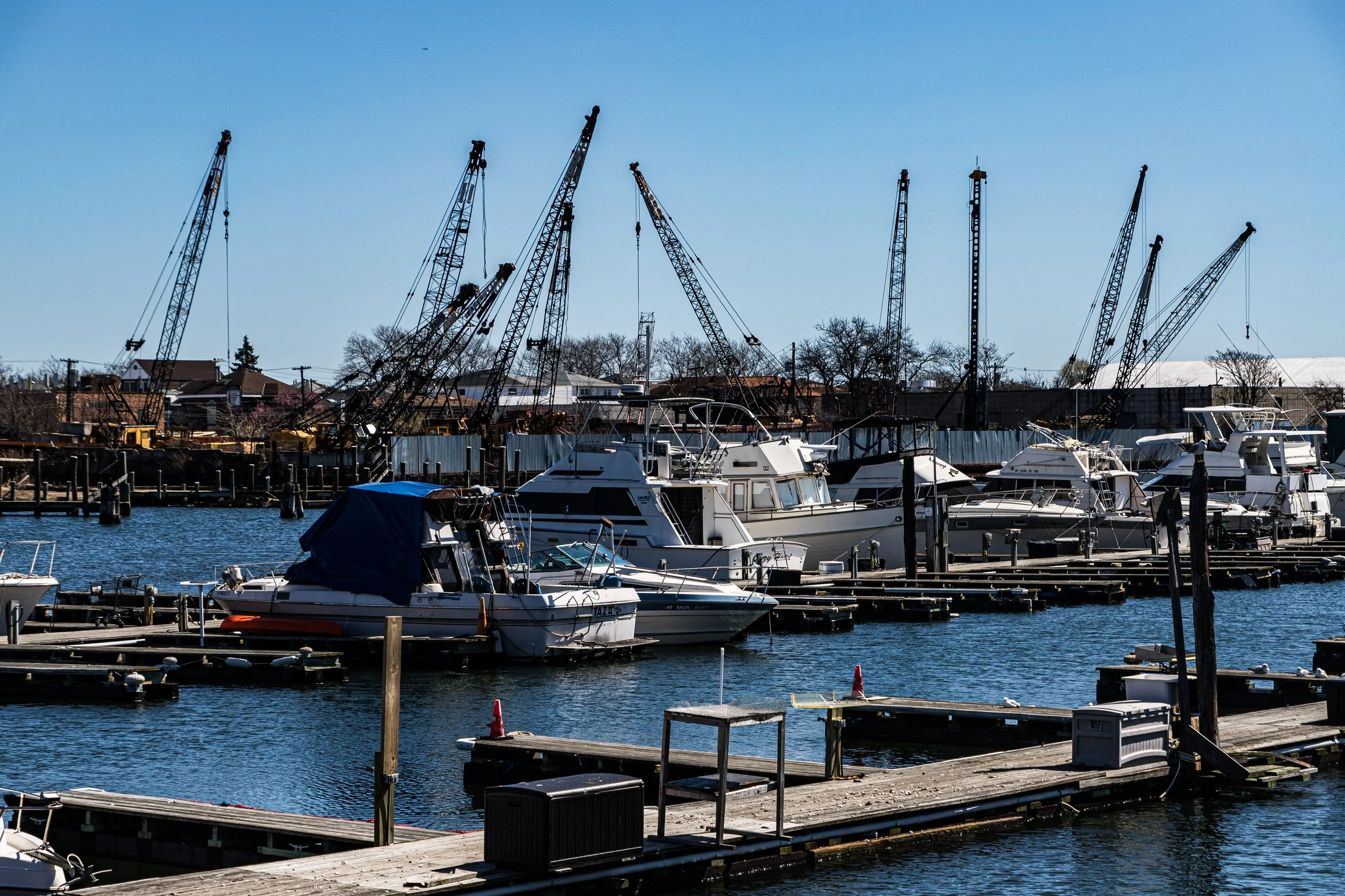 Yachts and boats docked at a marina with construction cranes and buildings in the background.