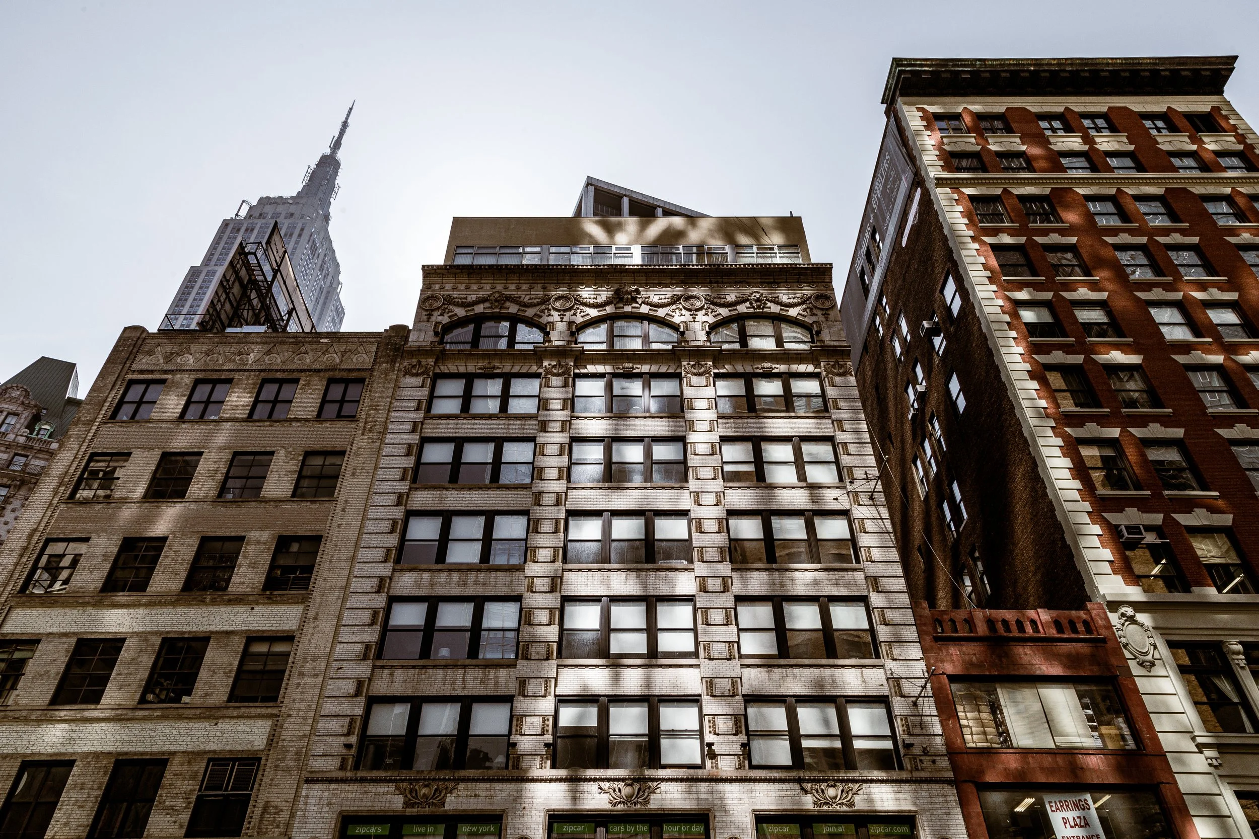 Low-angle view of multiple high-rise city buildings in New York City with the Empire State Building in the background.