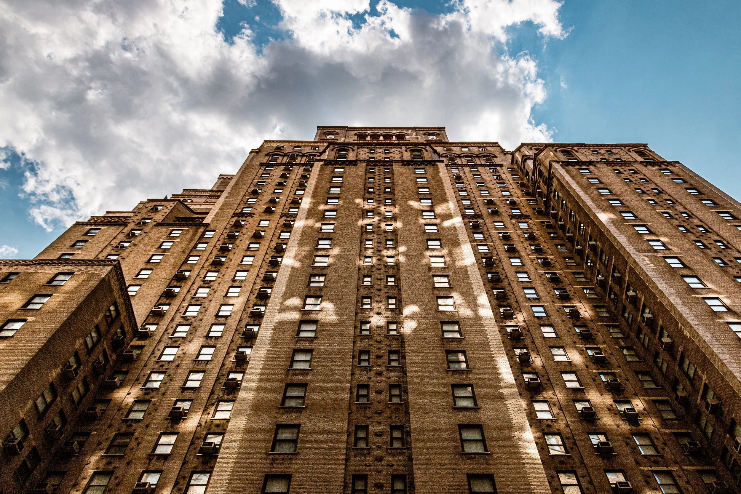 Looking up at a tall, old brick skyscraper with multiple windows and architectural details, under a partly cloudy sky.