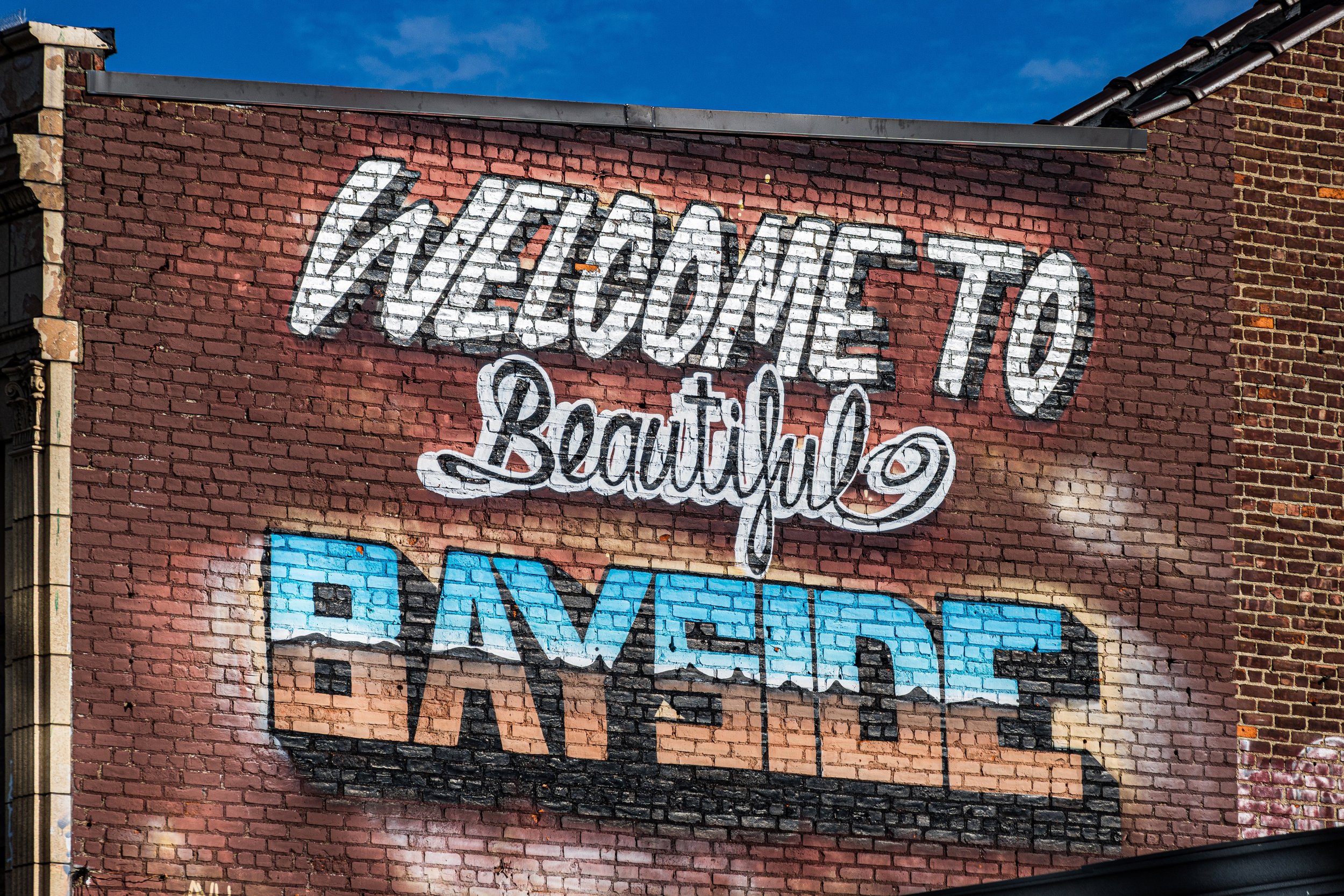 Colorful mural on brick wall reading 'Welcome to Beautiful Bayview' with vibrant blue, black, and pink colors.