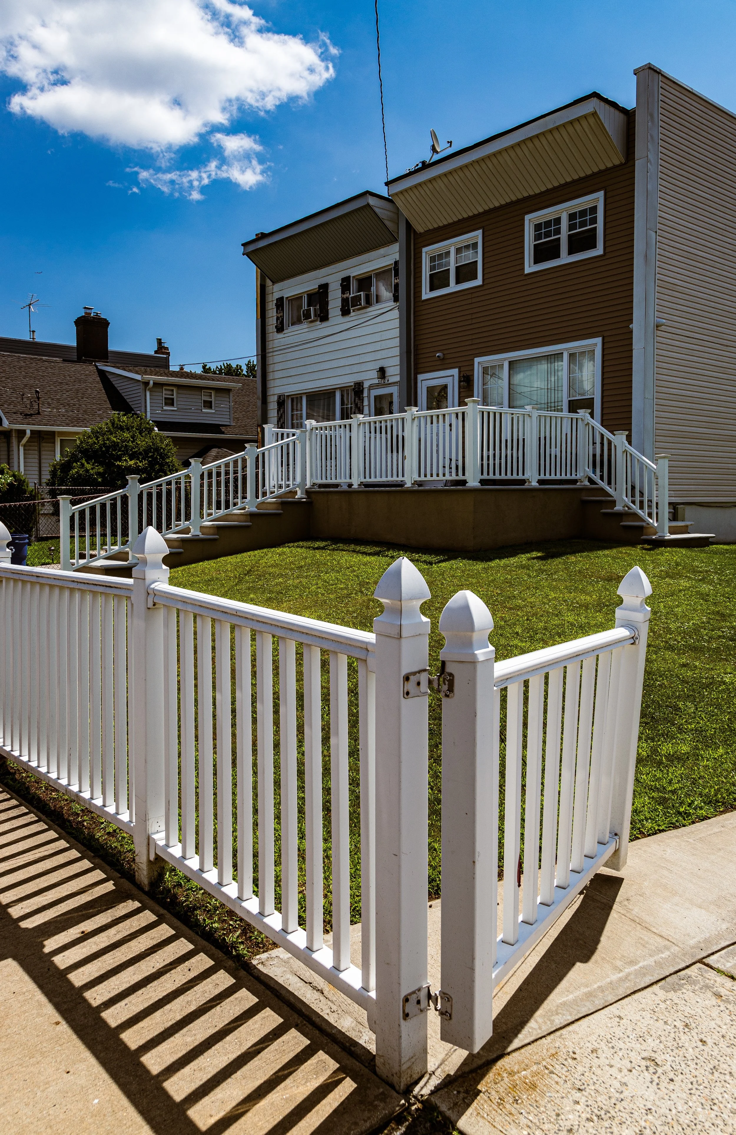 Backyard fence surrounding a grassy area with a house in the background under a partly cloudy sky.