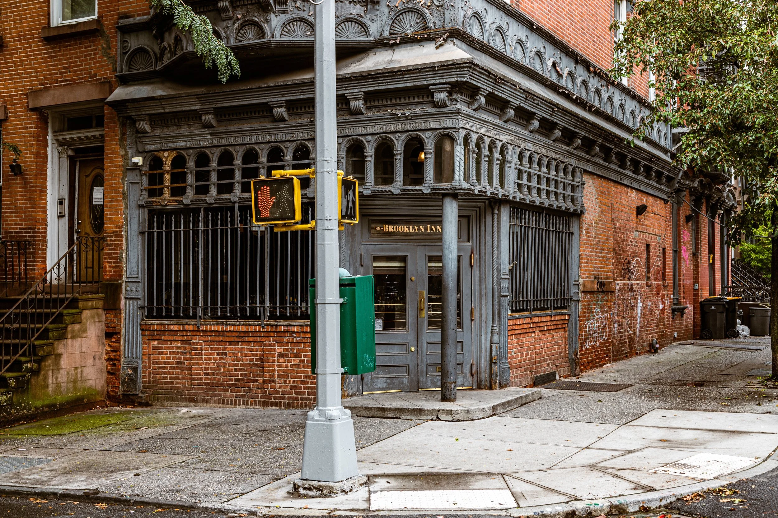 A corner building with old brick and ornate black metalwork, a sign reading 'Brooklyn Inn' above the entrance, a green mailbox, and a traffic light for pedestrians.