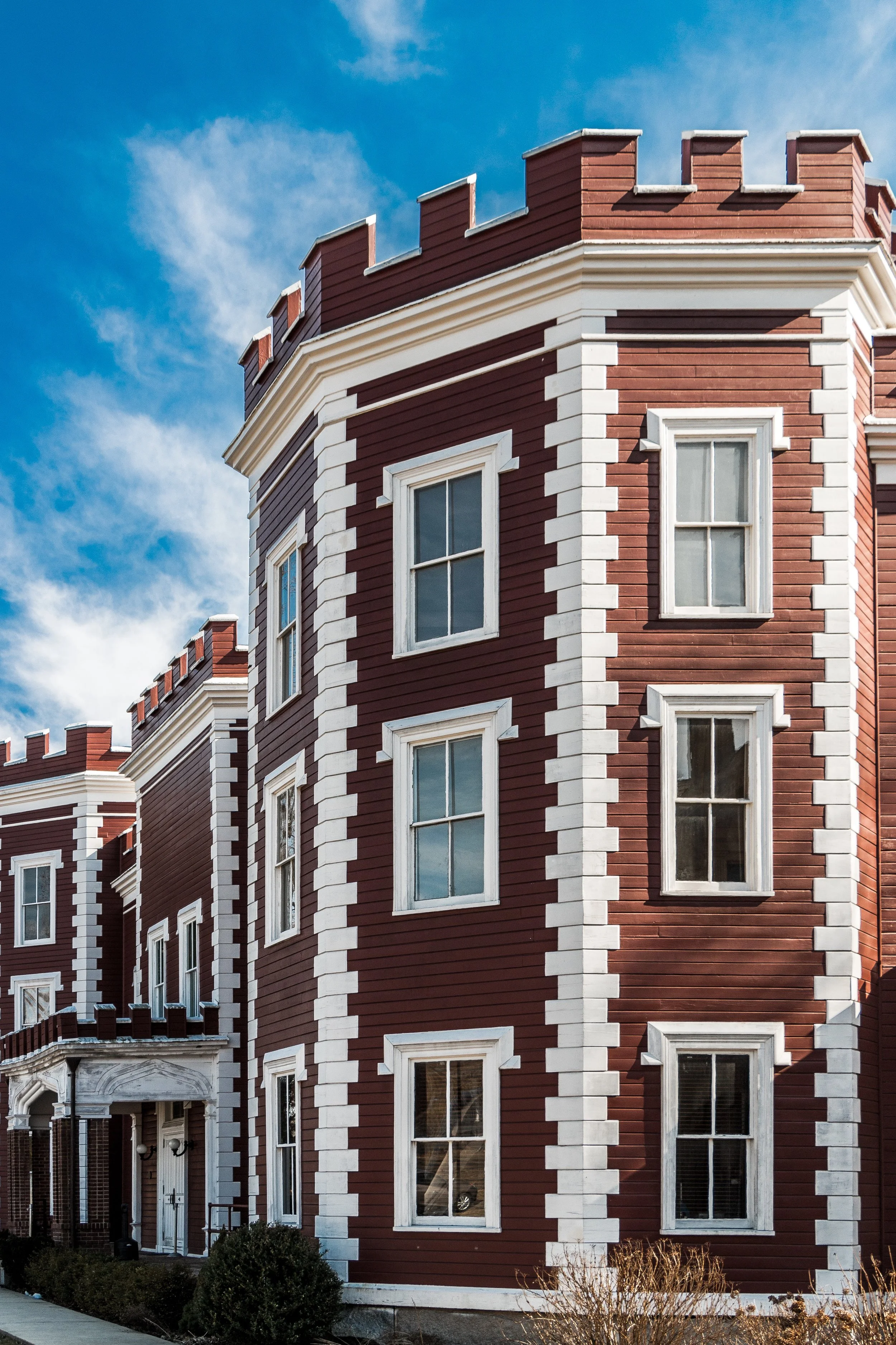Multi-story red brick building with white accents, archways, and multiple windows, under a partly cloudy blue sky.
