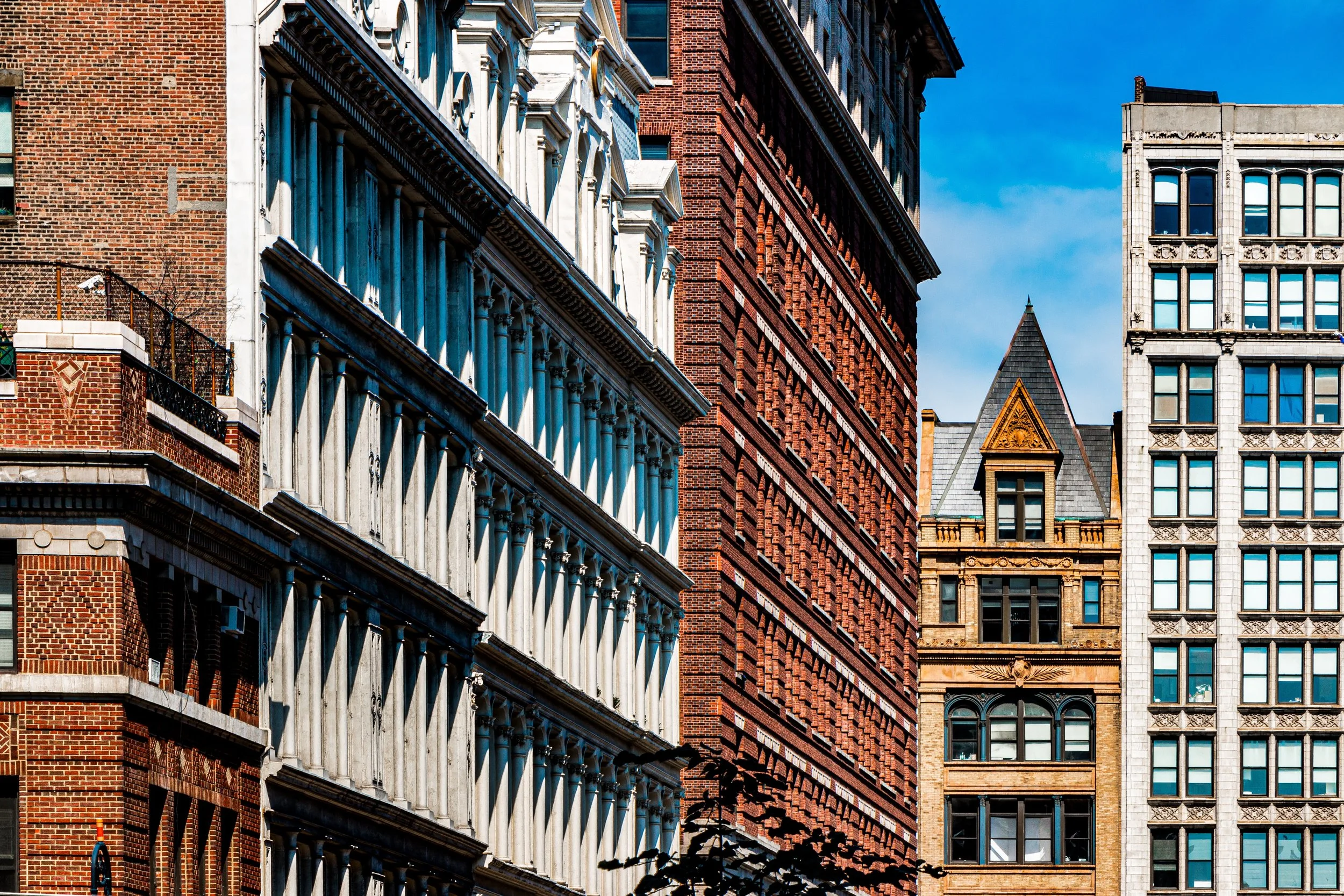 Close-up of several tall buildings in New York City, showcasing varied architectural styles with brick and stone facades, and clear blue sky in the background.