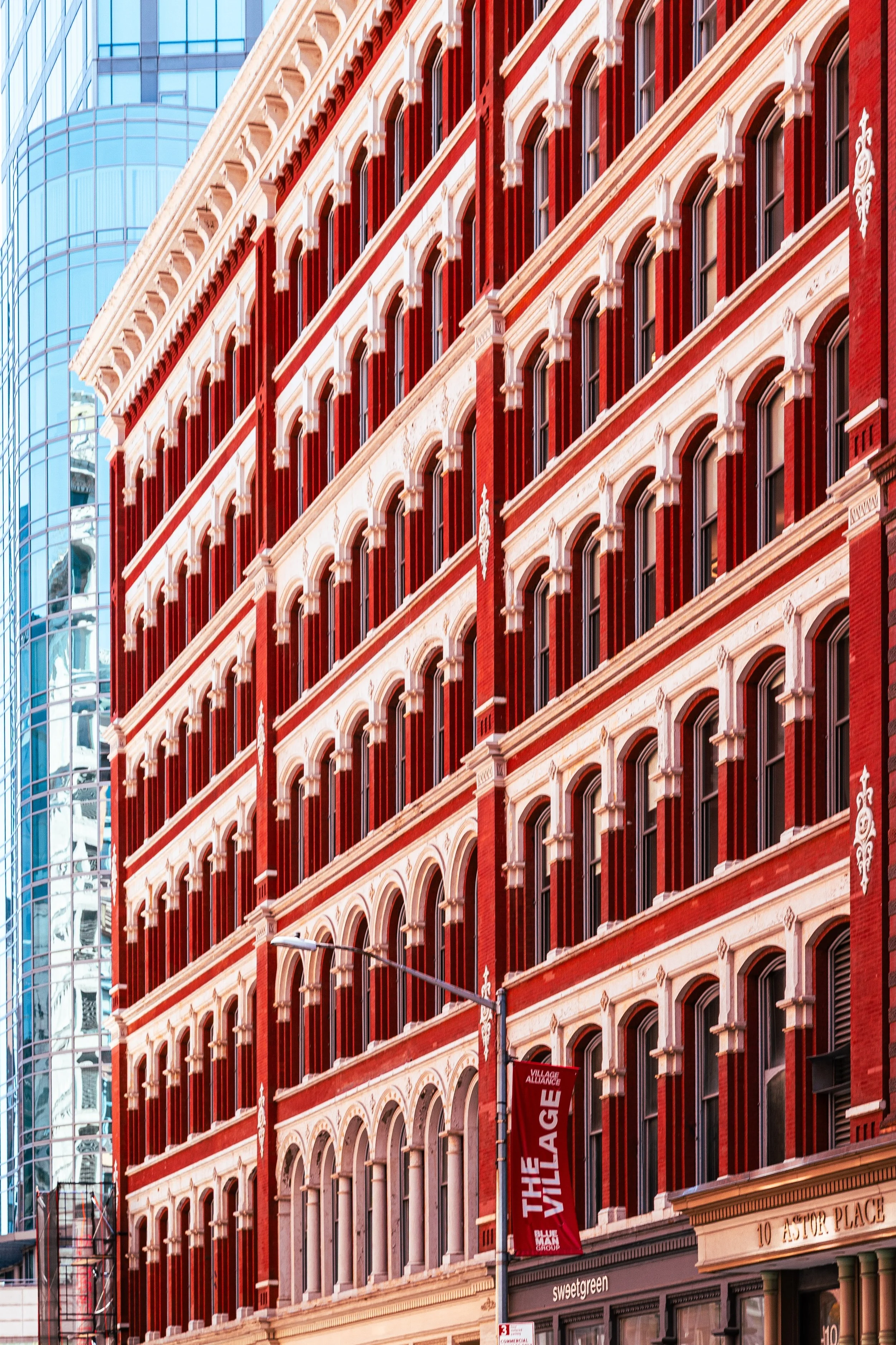 Red brick building with multiple floors featuring arched windows and decorative elements, located on a city street with a lamppost and nearby modern glass building.