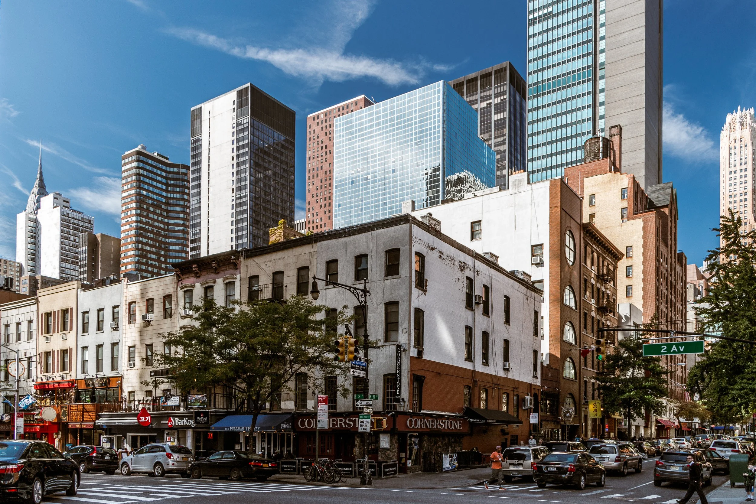 City street scene with historic low-rise buildings at the corner and modern skyscrapers in the background on a sunny day.