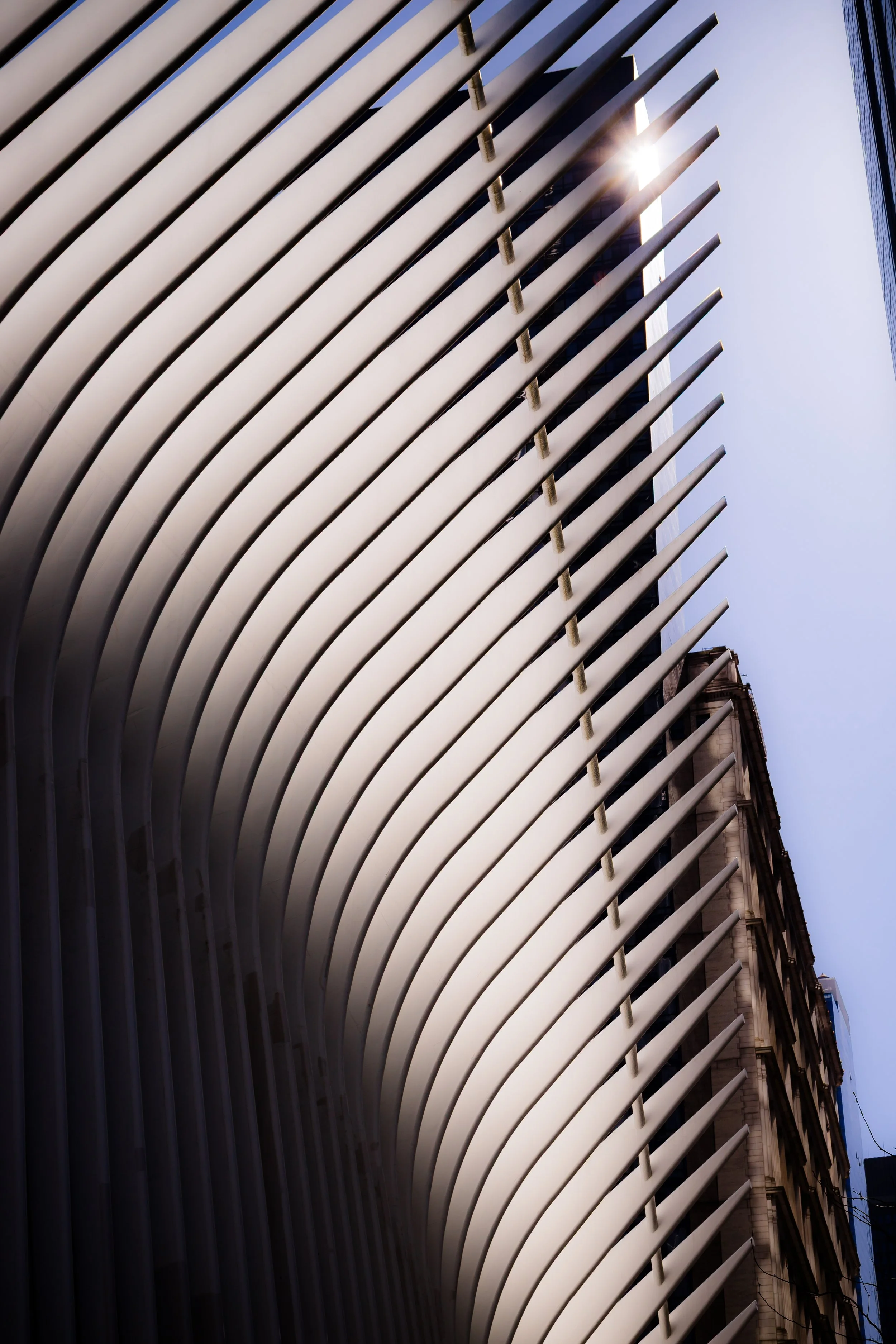 Close-up of a modern building with curved white horizontal slats on the facade, with sunlight shining through.
