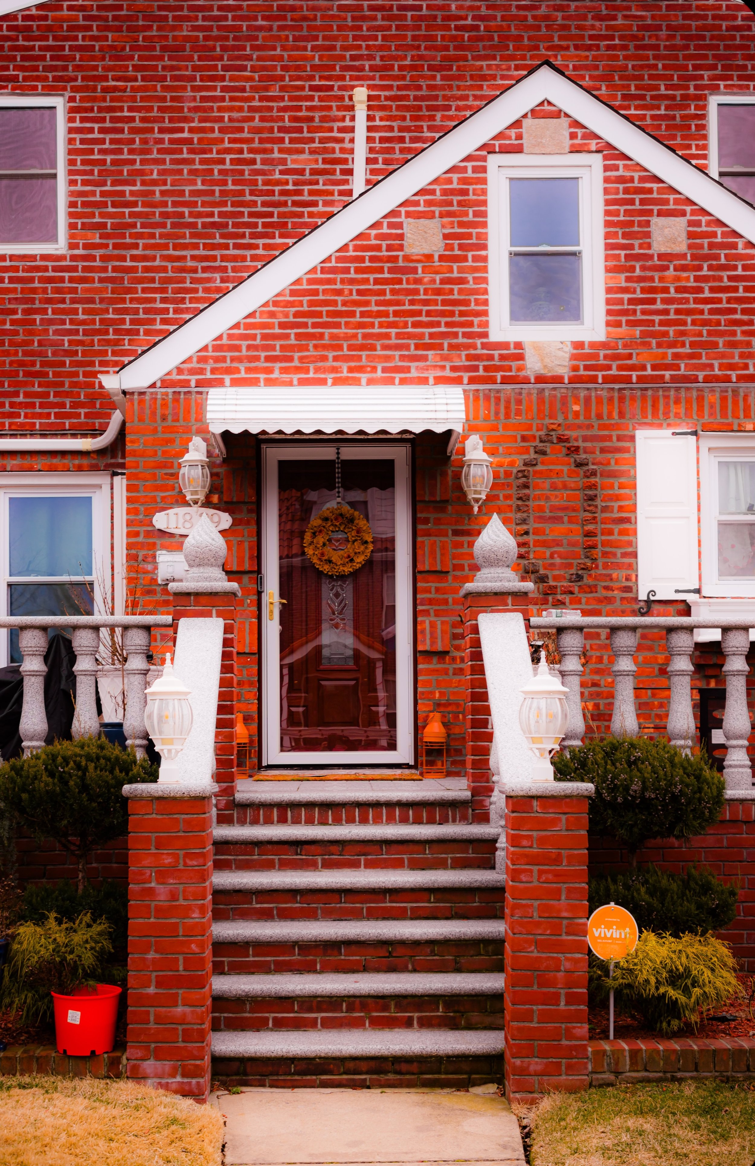 Front view of a brick house with a porch, stairs, and decorative lamps.