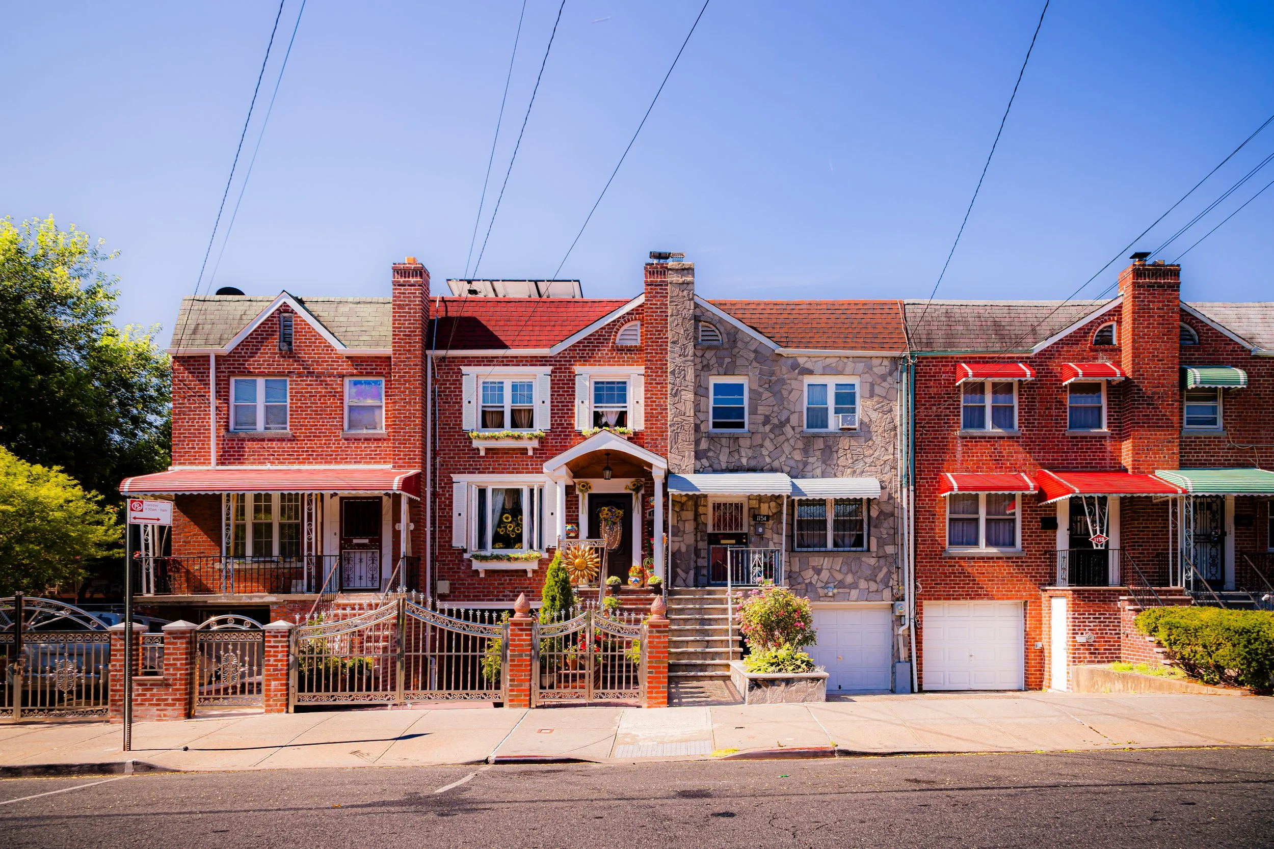 Row of attached brick houses on a sunny street, with front steps, gardens, and colorful awnings.