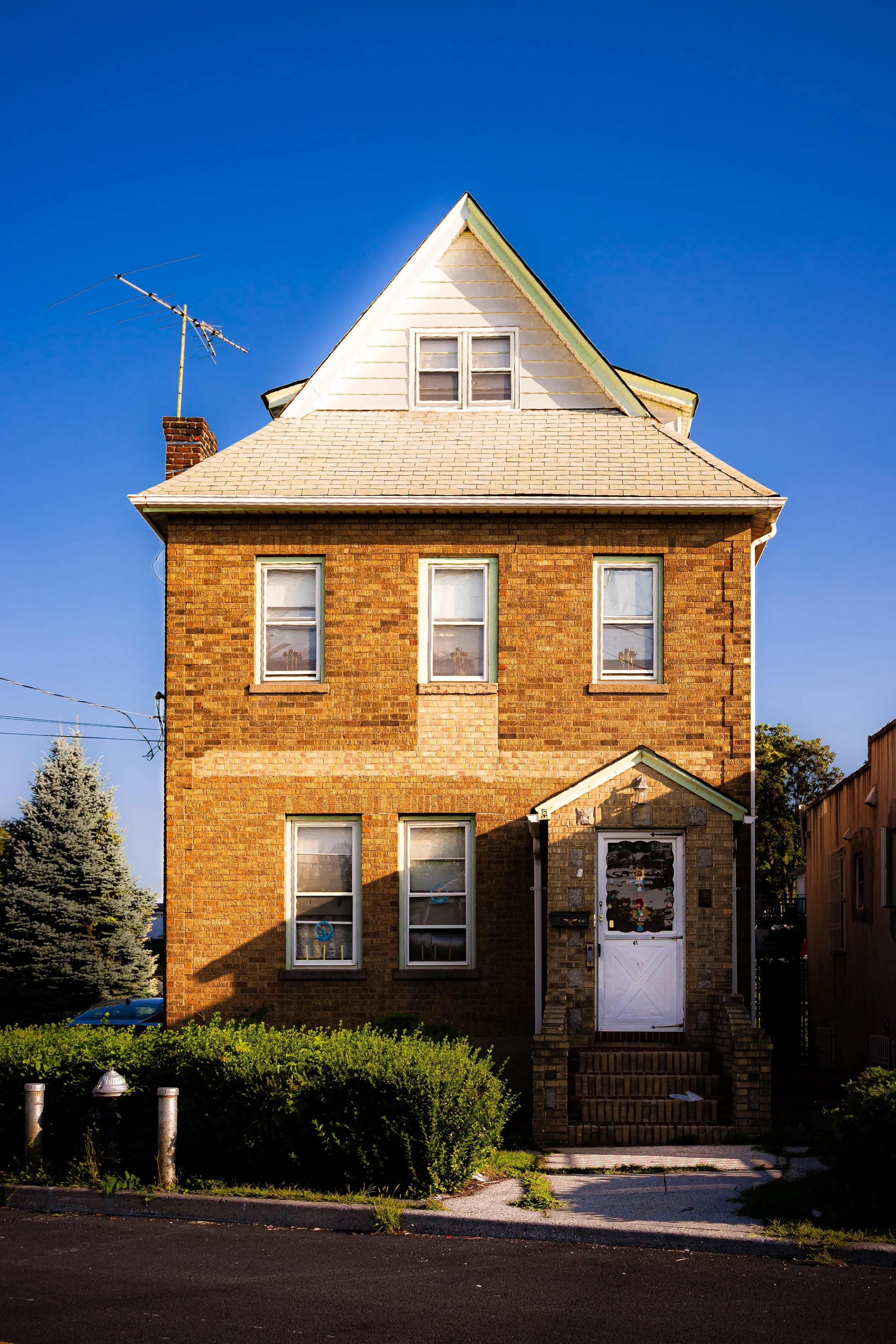 A three-story brick house with a pitched roof and a front porch, set against a clear blue sky.