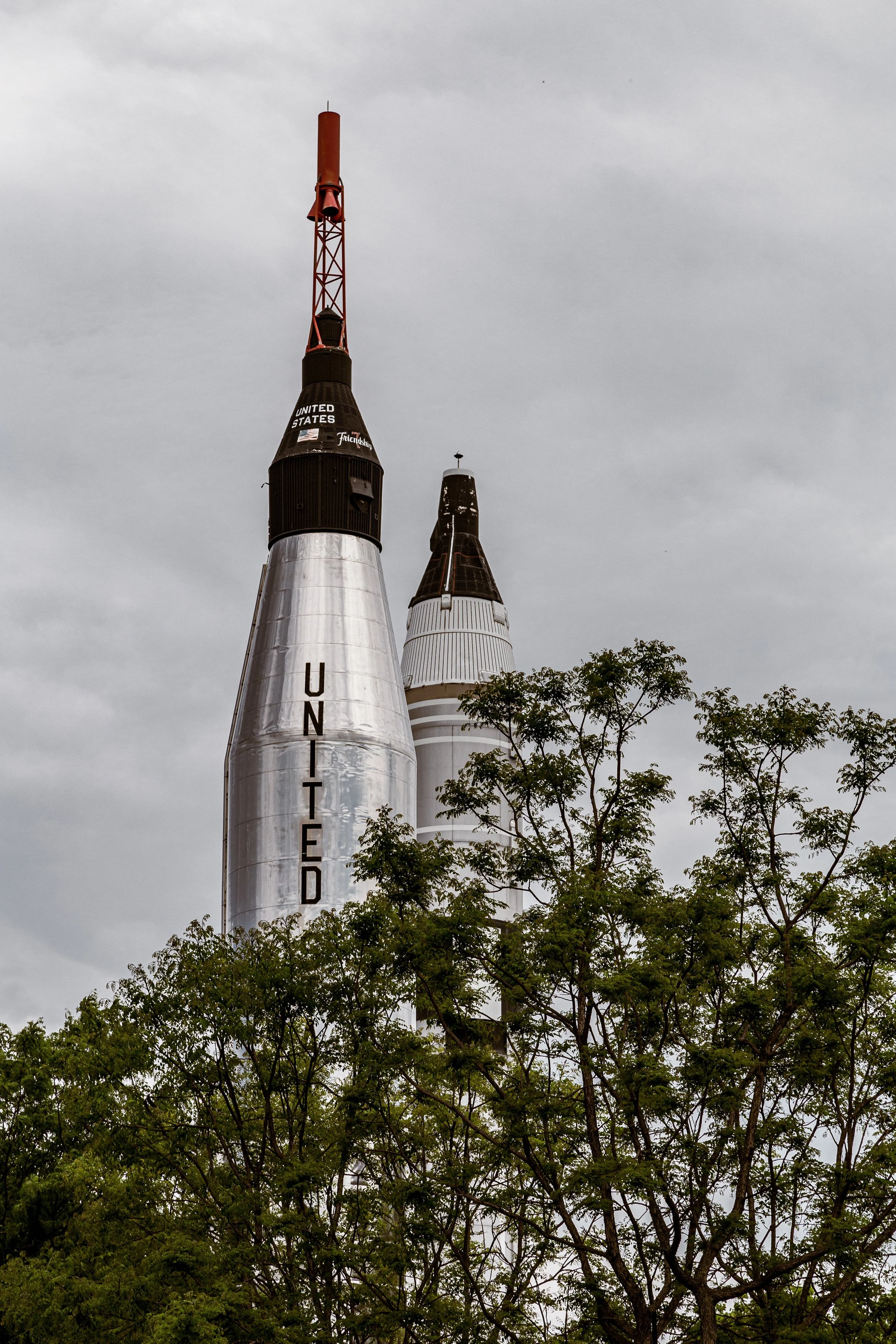 A spacecraft resembling a rocket, partially obscured by trees, with the words 'UNITED' and 'STATES' visible on it.