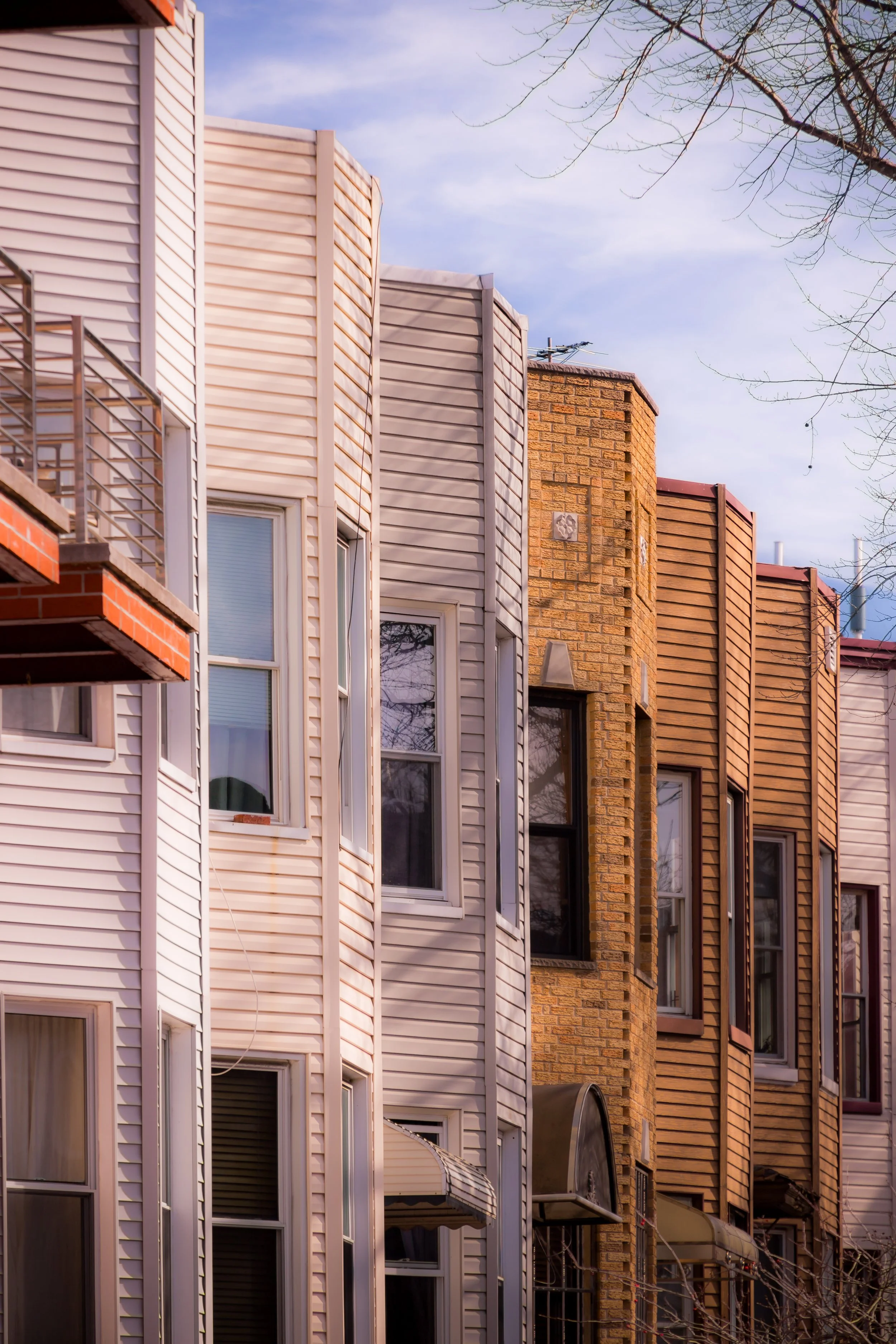 Close-up view of the facades of multiple residential buildings with various siding materials, windows, and balconies against a partly cloudy sky.