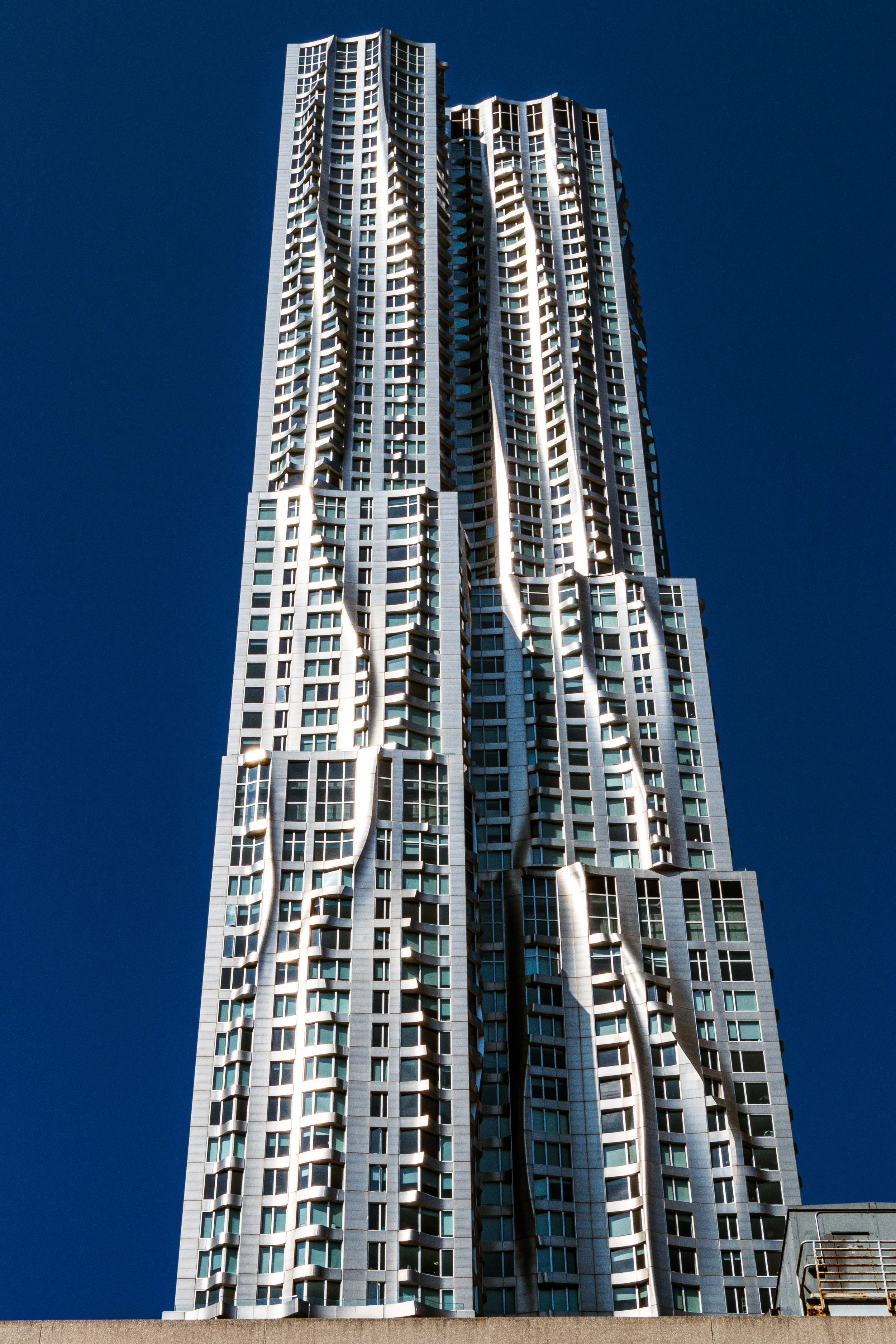 A tall modern skyscraper with a unique, wavy architectural design and numerous windows, set against a clear blue sky.