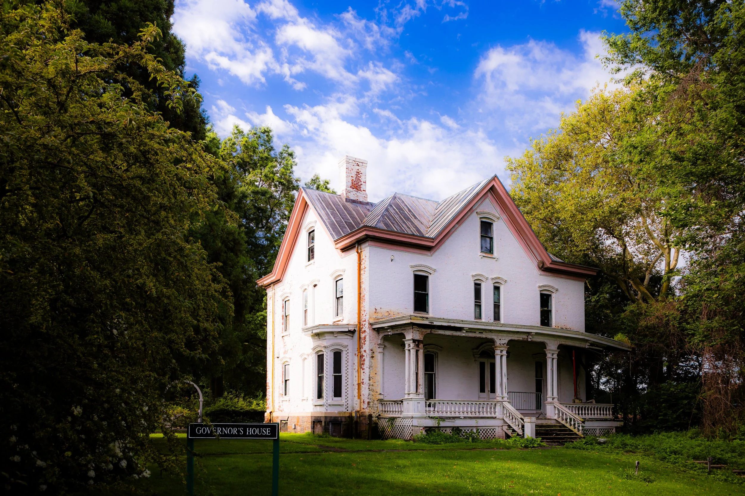 White historic house labeled as 'Governor's House' surrounded by green trees and grass under a partly cloudy blue sky.