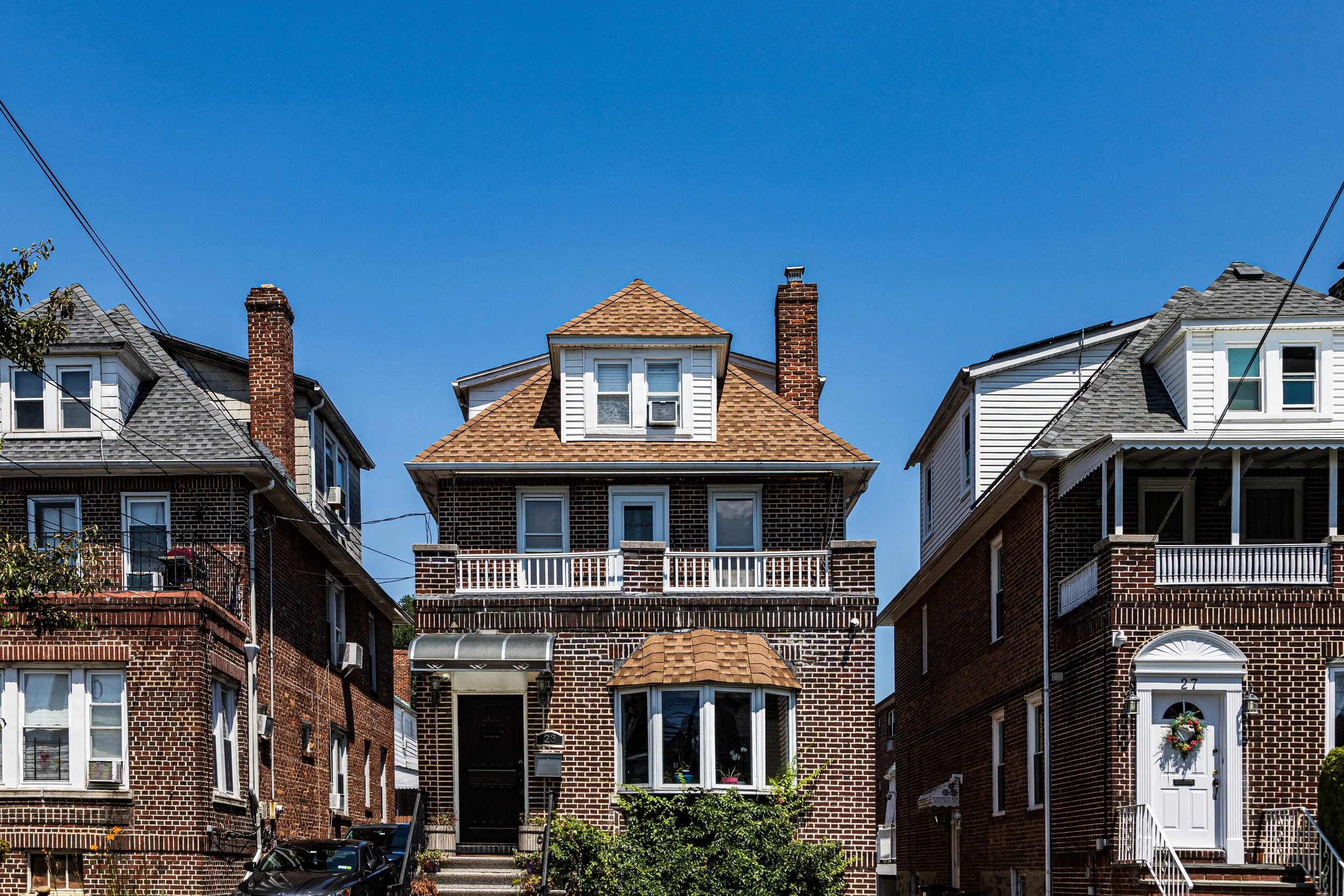 Three brick houses with peaked roofs and chimneys, front porches, and bay windows, under a clear blue sky.