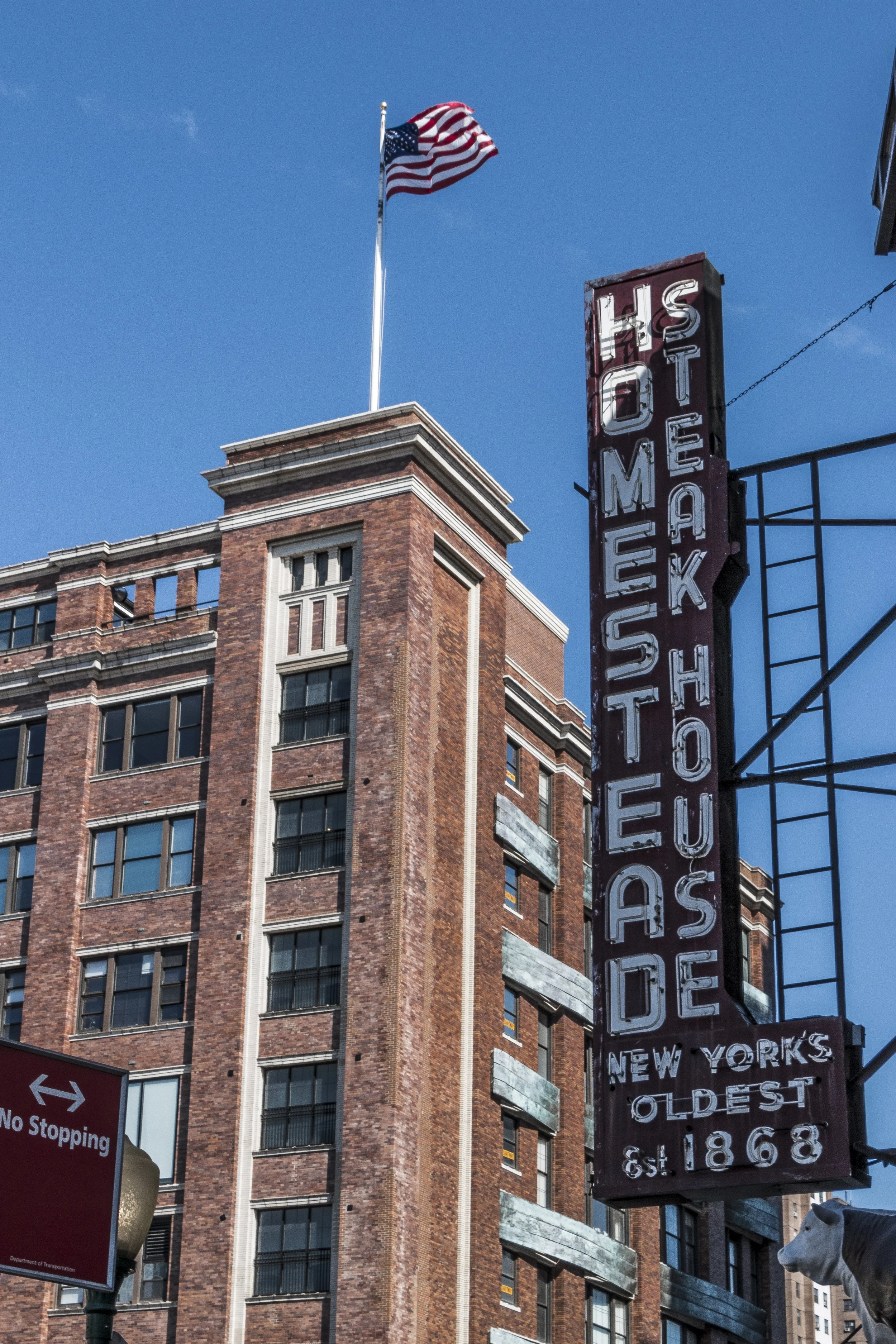 Historic brick building with an American flag on top and a vertical sign that reads 'HOMESTEAD S HOUS E'.