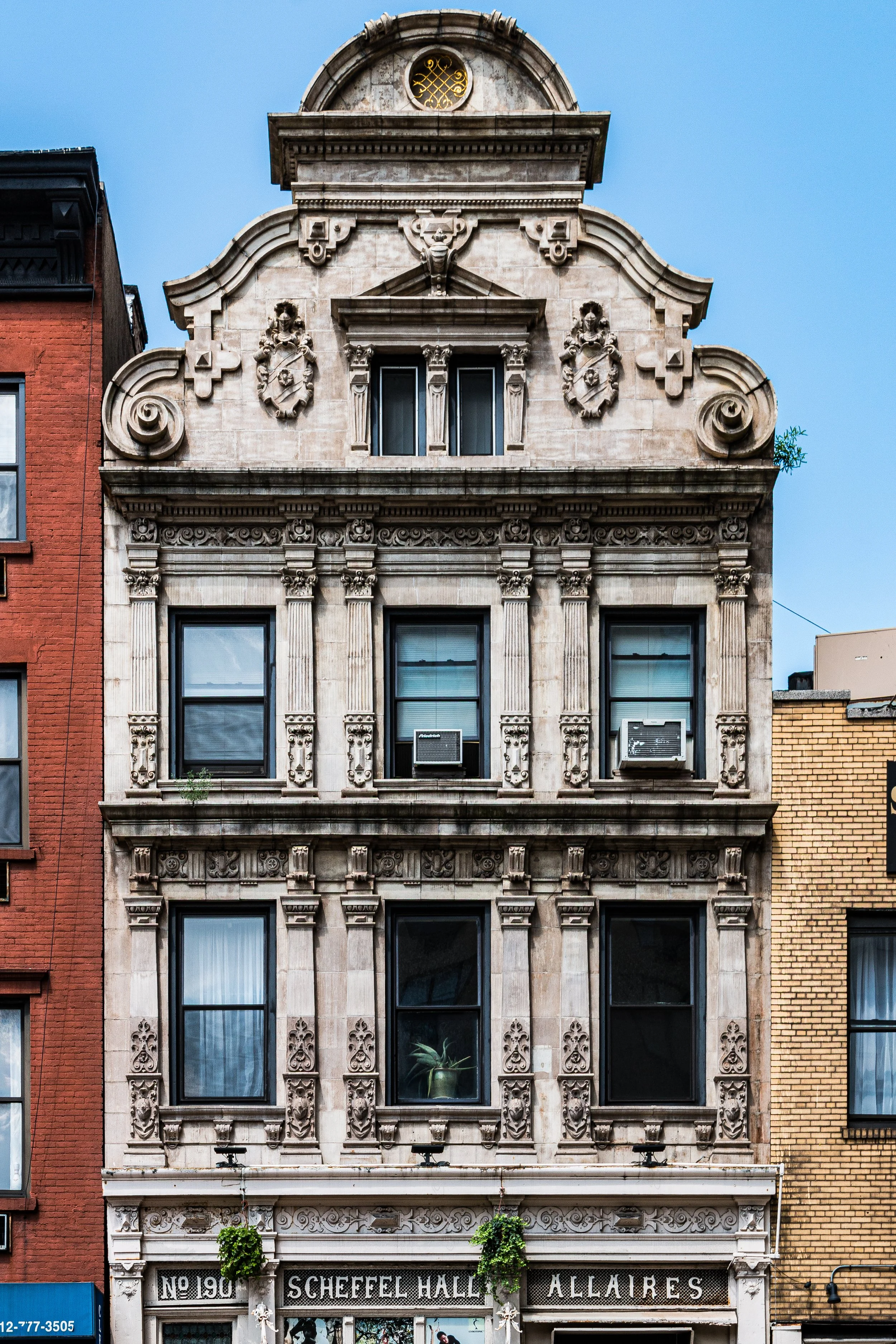 A historic building with ornate architectural details, multiple windows, and decorative elements on a city street, with neighboring buildings on each side.