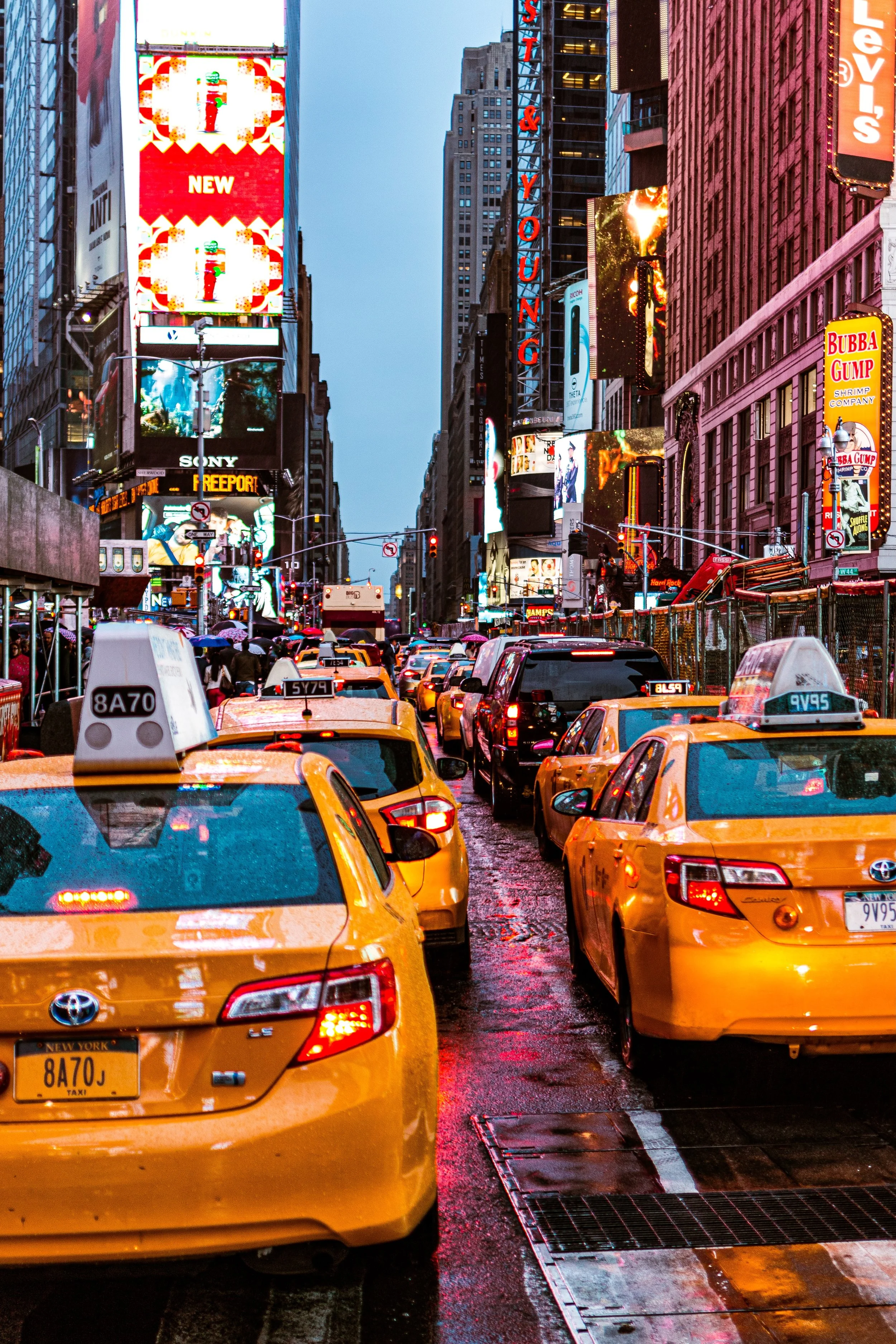 Busy street scene in Times Square, New York City, with yellow taxis, bright electronic billboards, and tall buildings.
