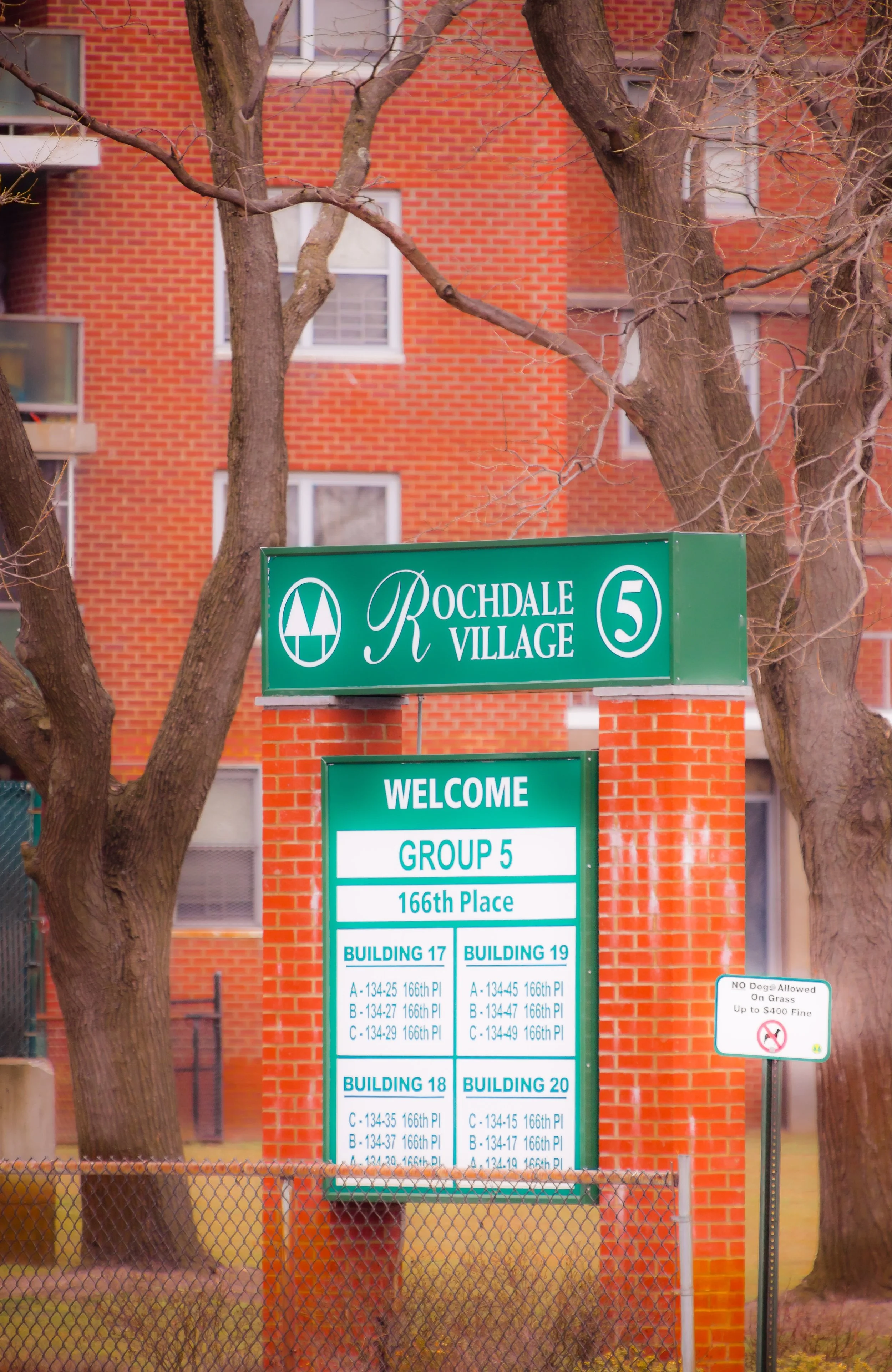 Sign for Rochdale Village with group and building information, and a smaller sign indicating no dogs allowed on grass with a fine.